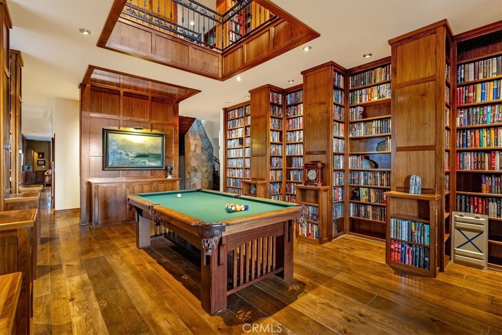 Library and billiards room with tall wooden bookshelves, a green-felt pool table, and a mezzanine.