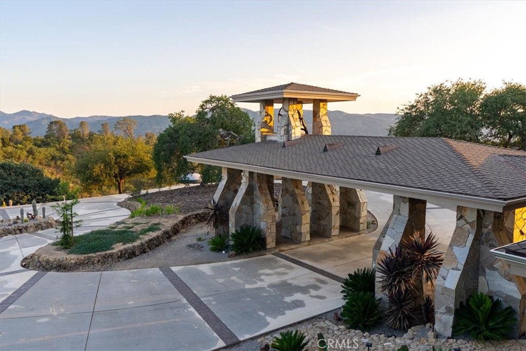 Stone-columned home entrance beside a landscaped driveway, with mountain ridges beyond.