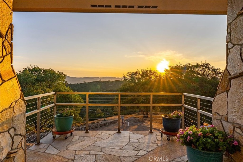 Stone patio overlooking wooded hills at sunset, framed by stone columns and potted flowers.