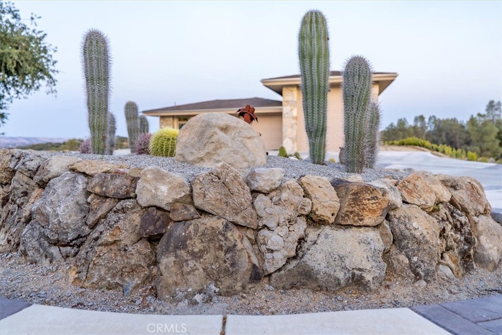 Home behind a stone retaining wall with tall cacti and gravel landscaping.
