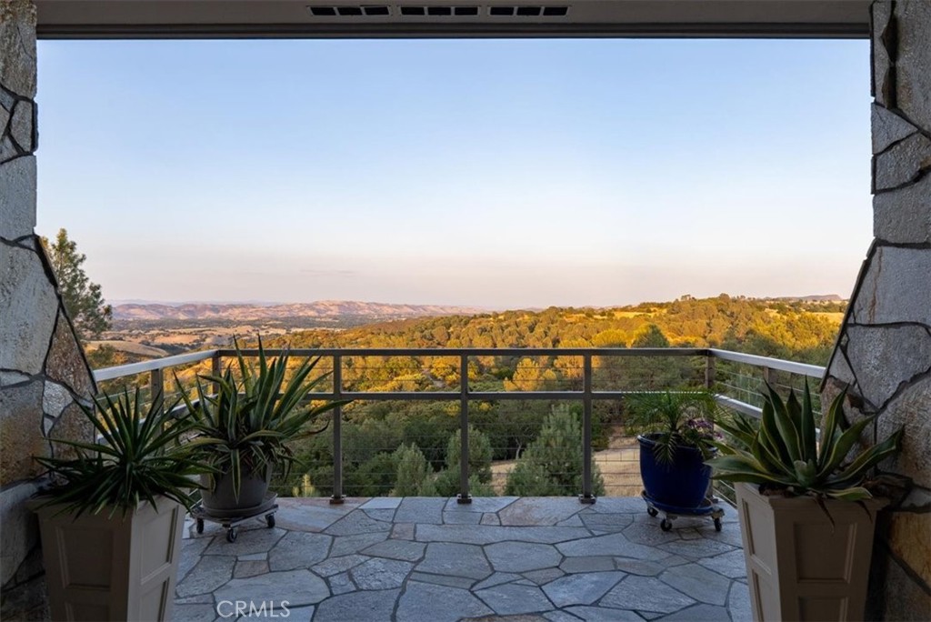 Stone patio with potted plants and a railing overlooking wooded rolling hills.
