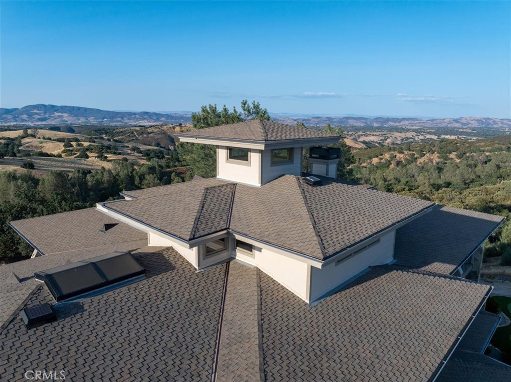 Aerial view of a home's broad tiled roof and solar panels, with rolling hills beyond.