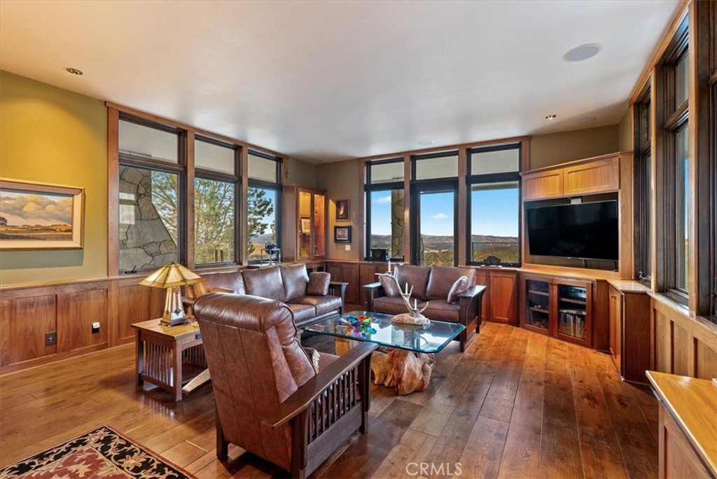 Living room with leather seating, wood paneling, and large windows overlooking rolling hills.