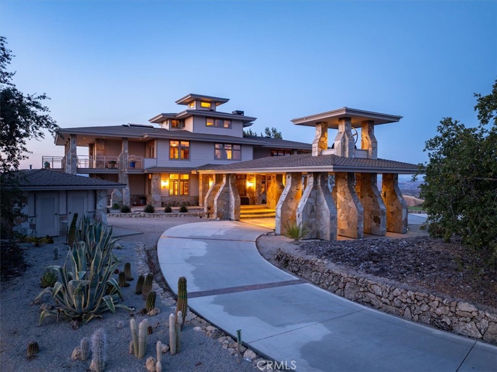 Multi-level home at dusk with illuminated windows, stone columns, and a curved driveway.
