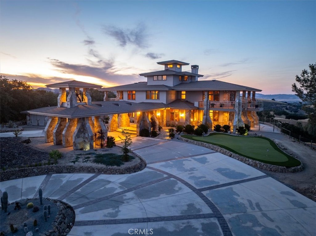 Multi-level home with stone columns and a patterned driveway at dusk.