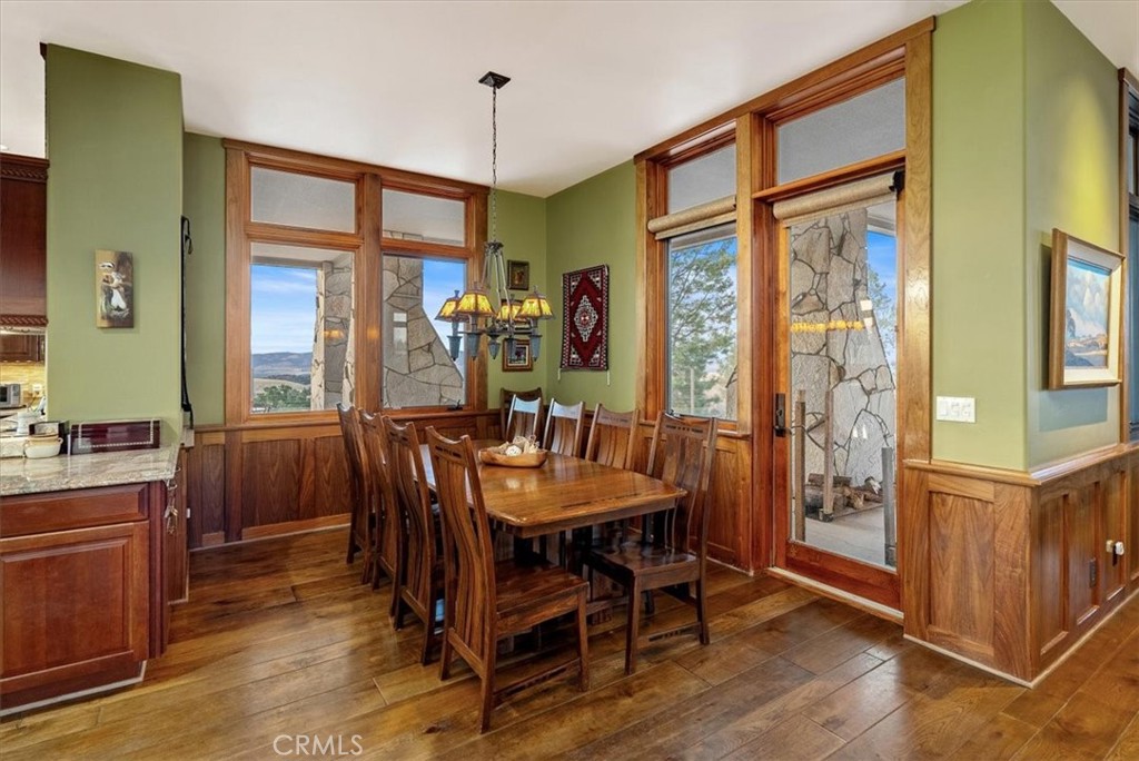Dining room with a long wooden table, rich wood trim, and tall windows overlooking distant hills.
