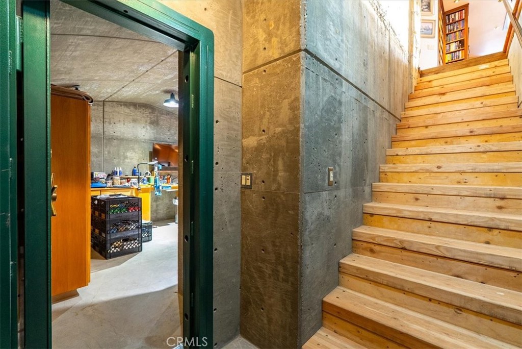 Wooden staircase beside exposed concrete walls, with an open doorway into a storage area.