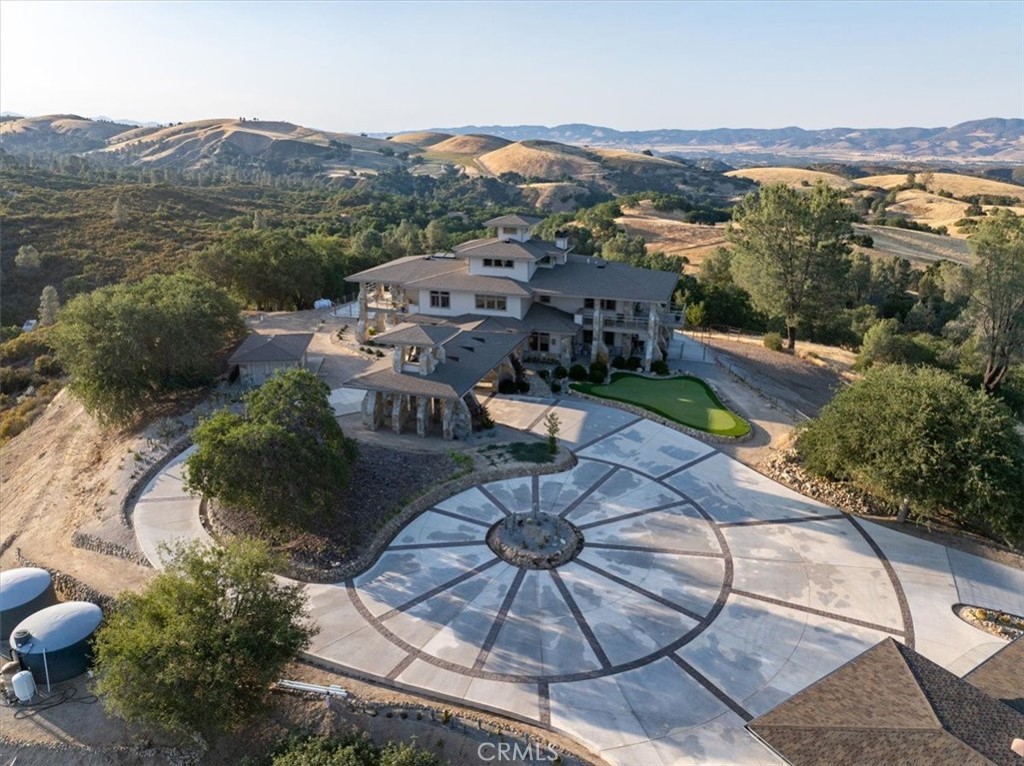 Large rural home with a circular patterned driveway, surrounded by trees and rolling hills.