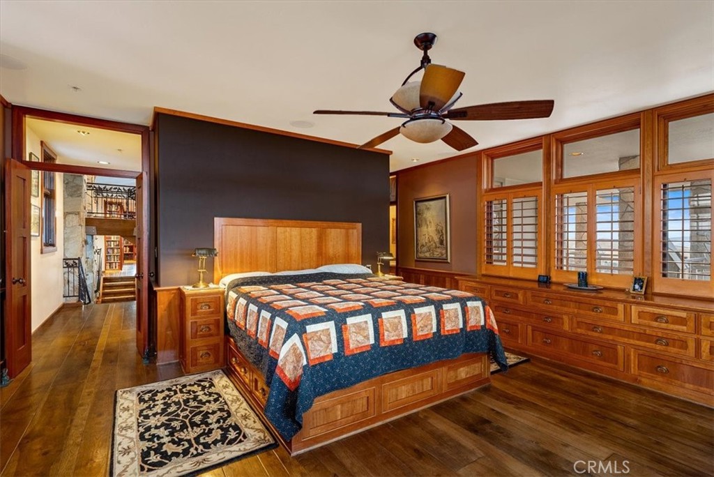 Bedroom with a wooden bed, colorful quilt, built-in drawers, and shuttered windows.