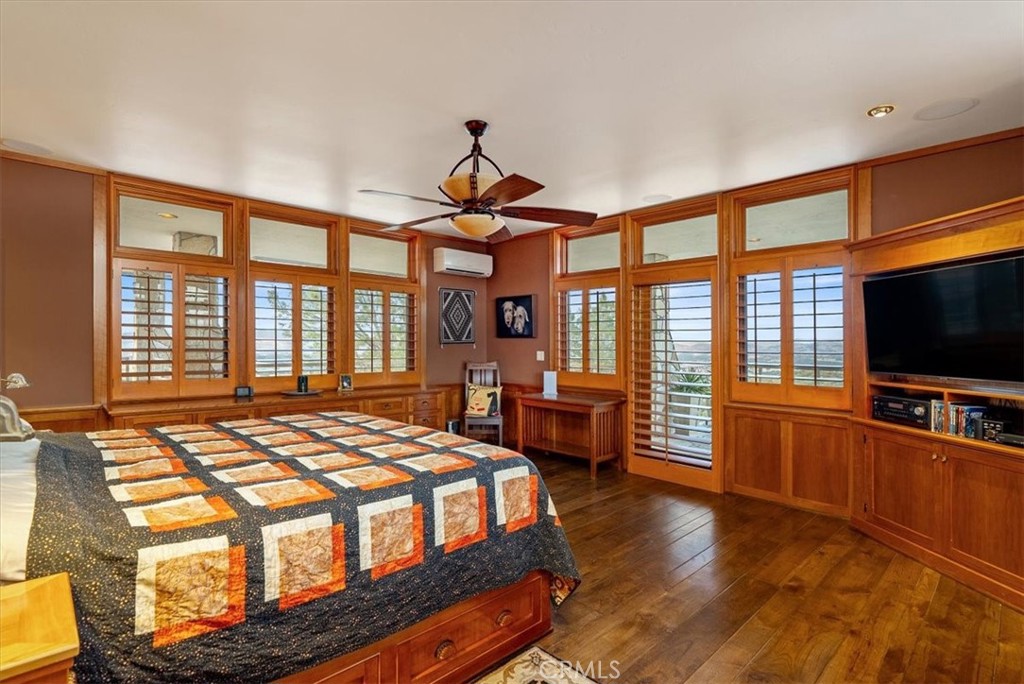 Bedroom with a patterned quilt, wood-trimmed windows, built-in cabinetry, and a ceiling fan.