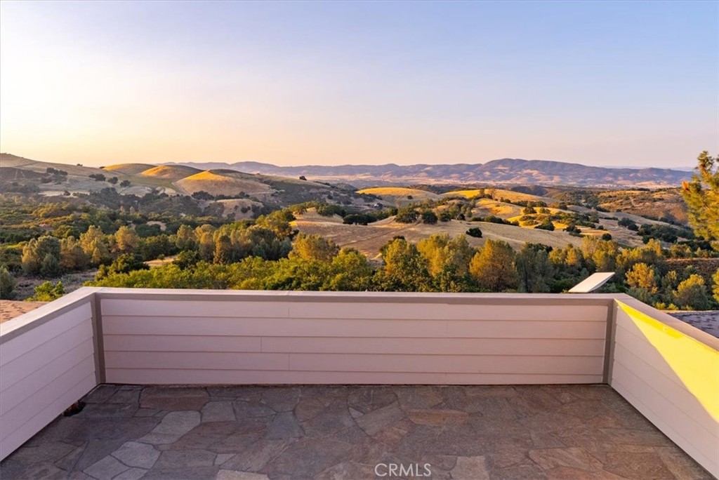 Stone-paved terrace overlooking rolling hills and wooded countryside in warm evening light.