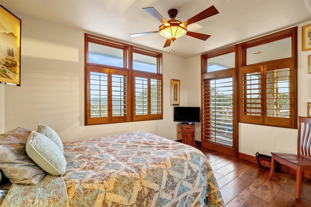 Bedroom with a large bed, wood-framed windows, plantation shutters, and views of distant hills.
