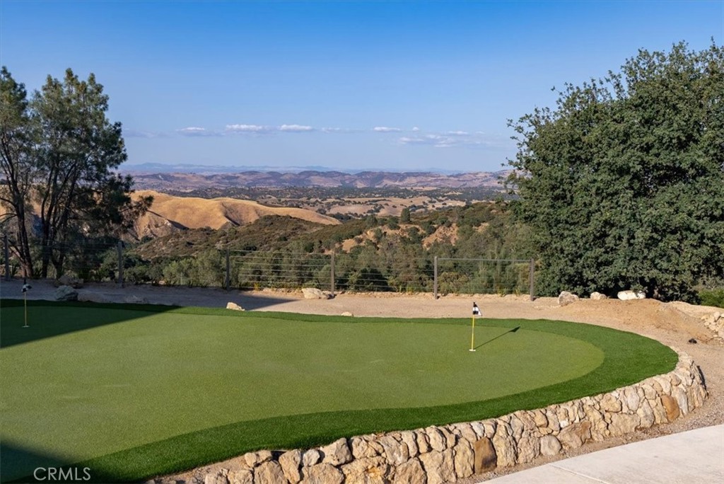 Outdoor putting green with two flagsticks and a stone retaining wall overlooking rolling hills.