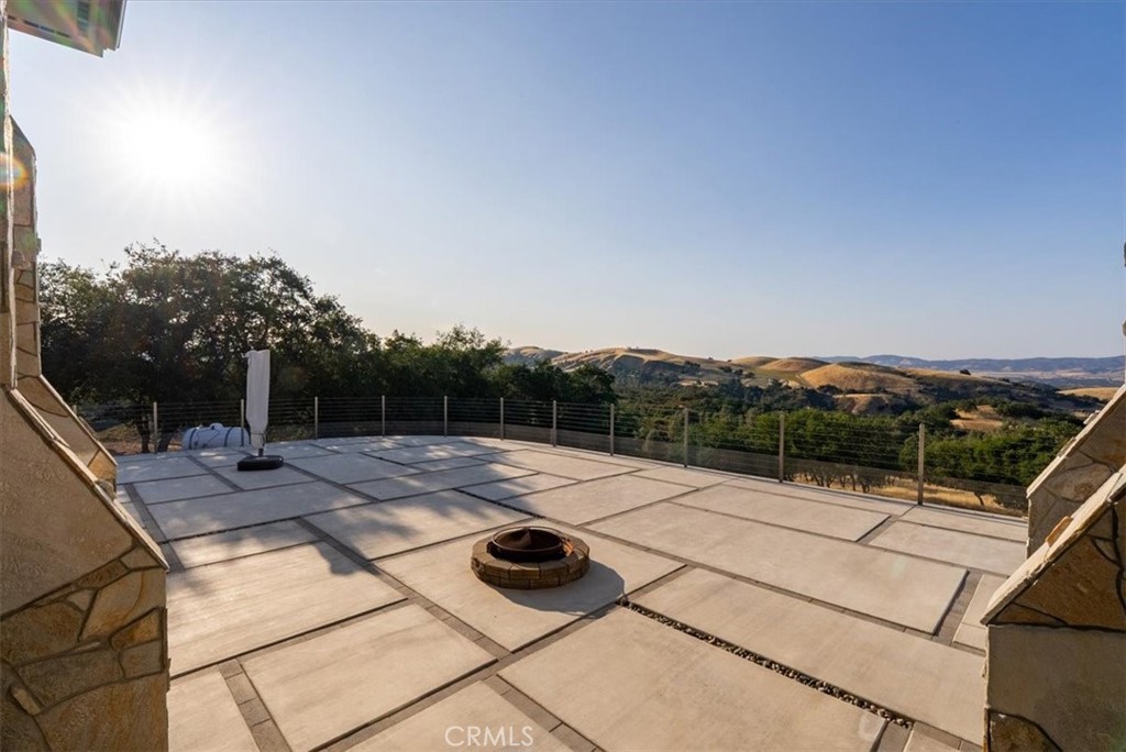 Paved patio with a circular fire pit and railing overlooking rolling hills.