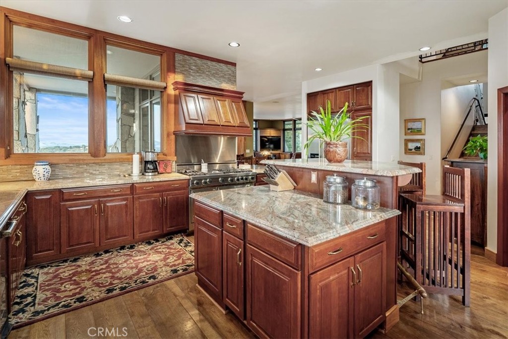 Kitchen with dark wood cabinetry, granite island, stainless steel range, and tall windows.