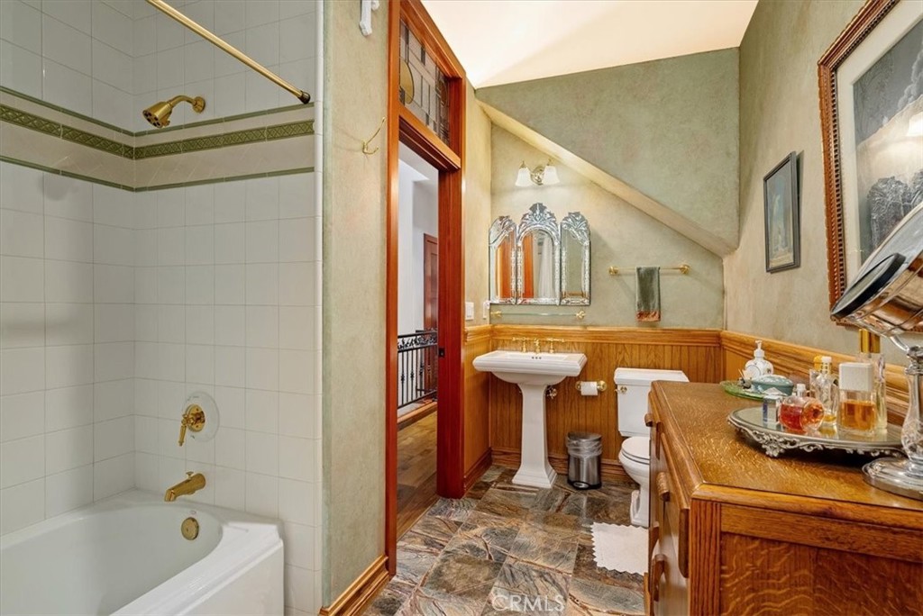 Bathroom with a tiled tub and shower, pedestal sink, and ornate wood vanity.