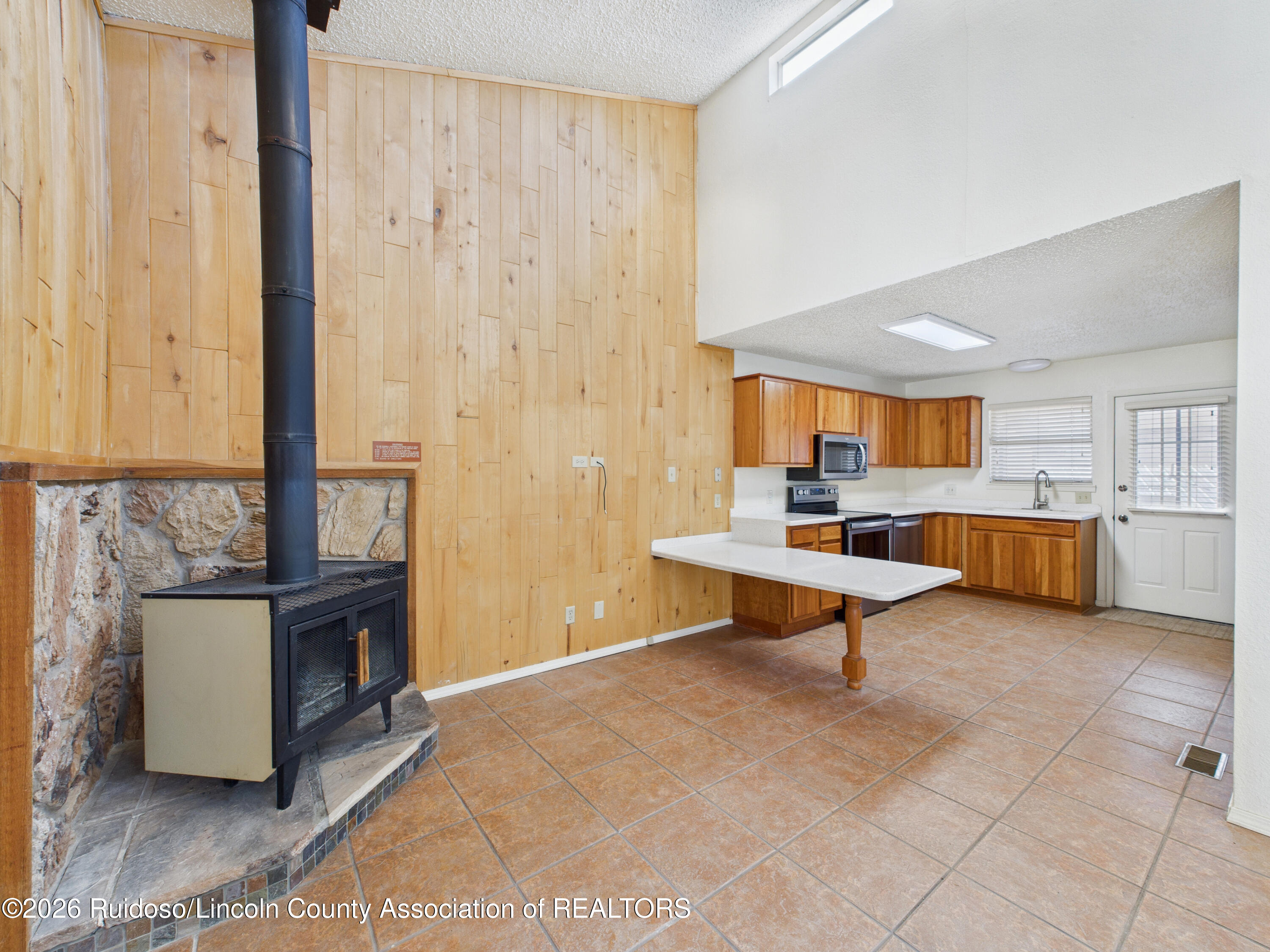 Kitchen with wood cabinets, a white peninsula, tiled floor, and a freestanding wood-burning stove.