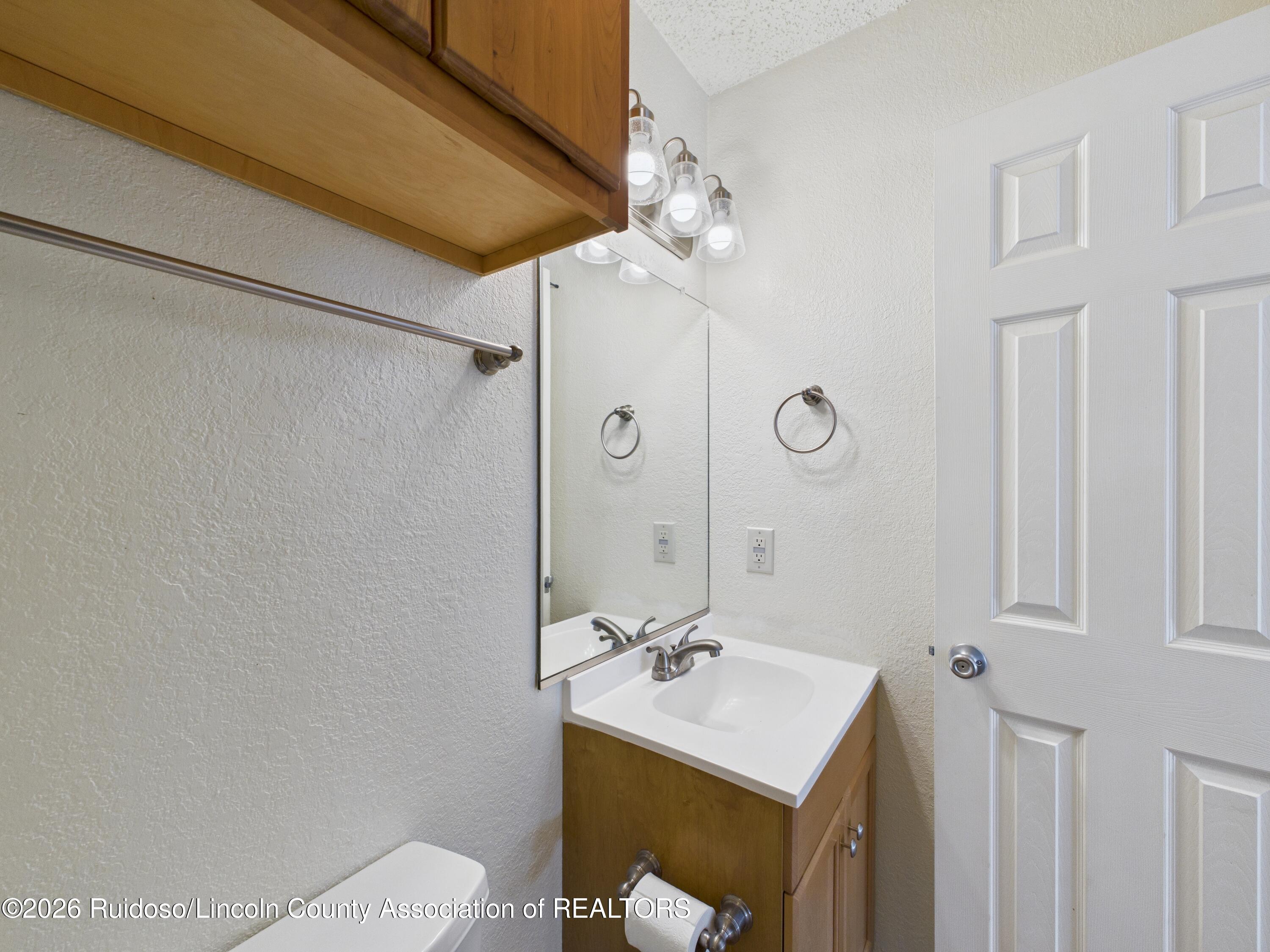 Bathroom vanity with a white sink, wood cabinetry, and a large mirror.