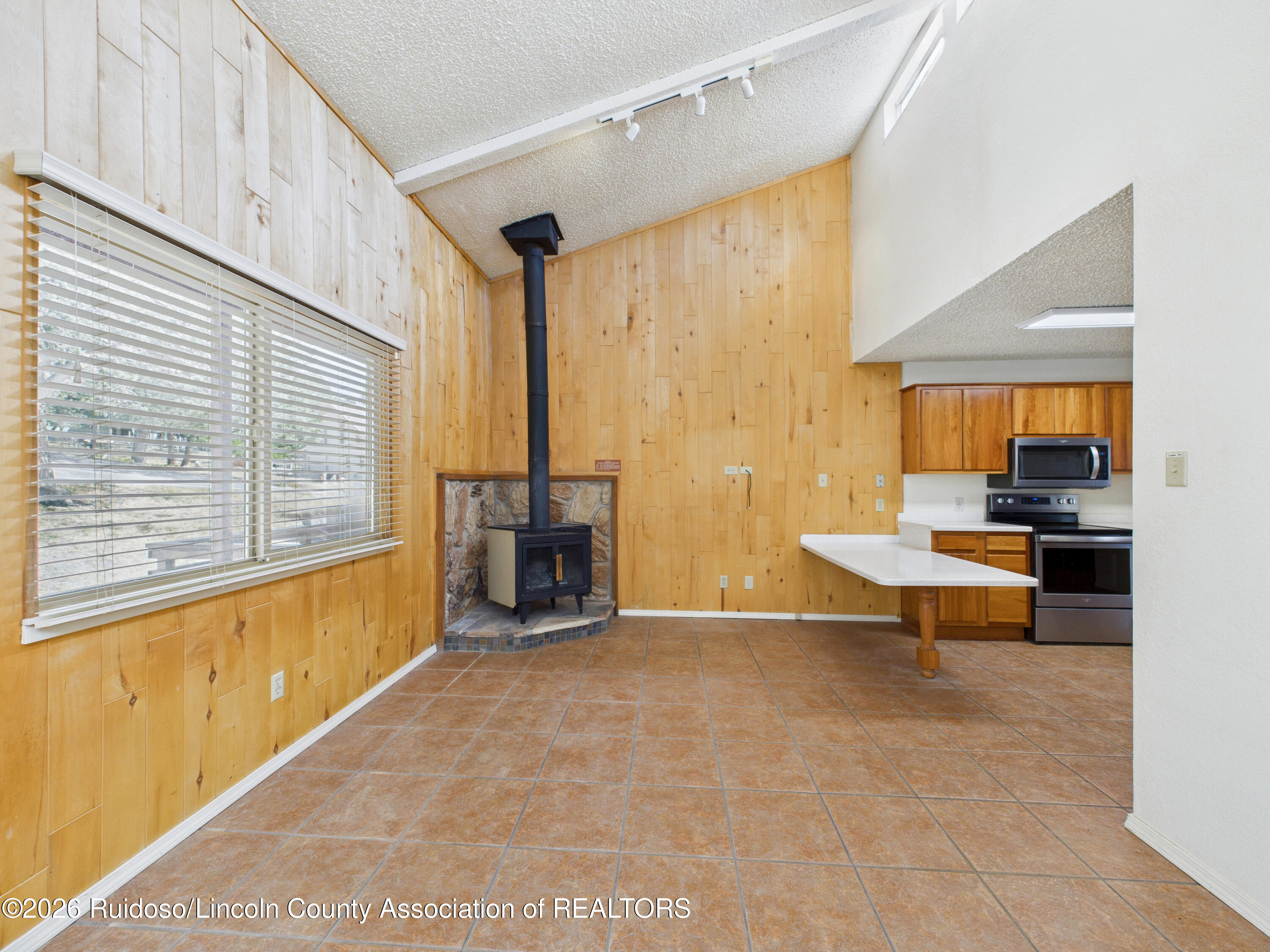Kitchen and living area with wood-paneled walls, a freestanding wood stove, tiled floors, and a kitchen peninsula.