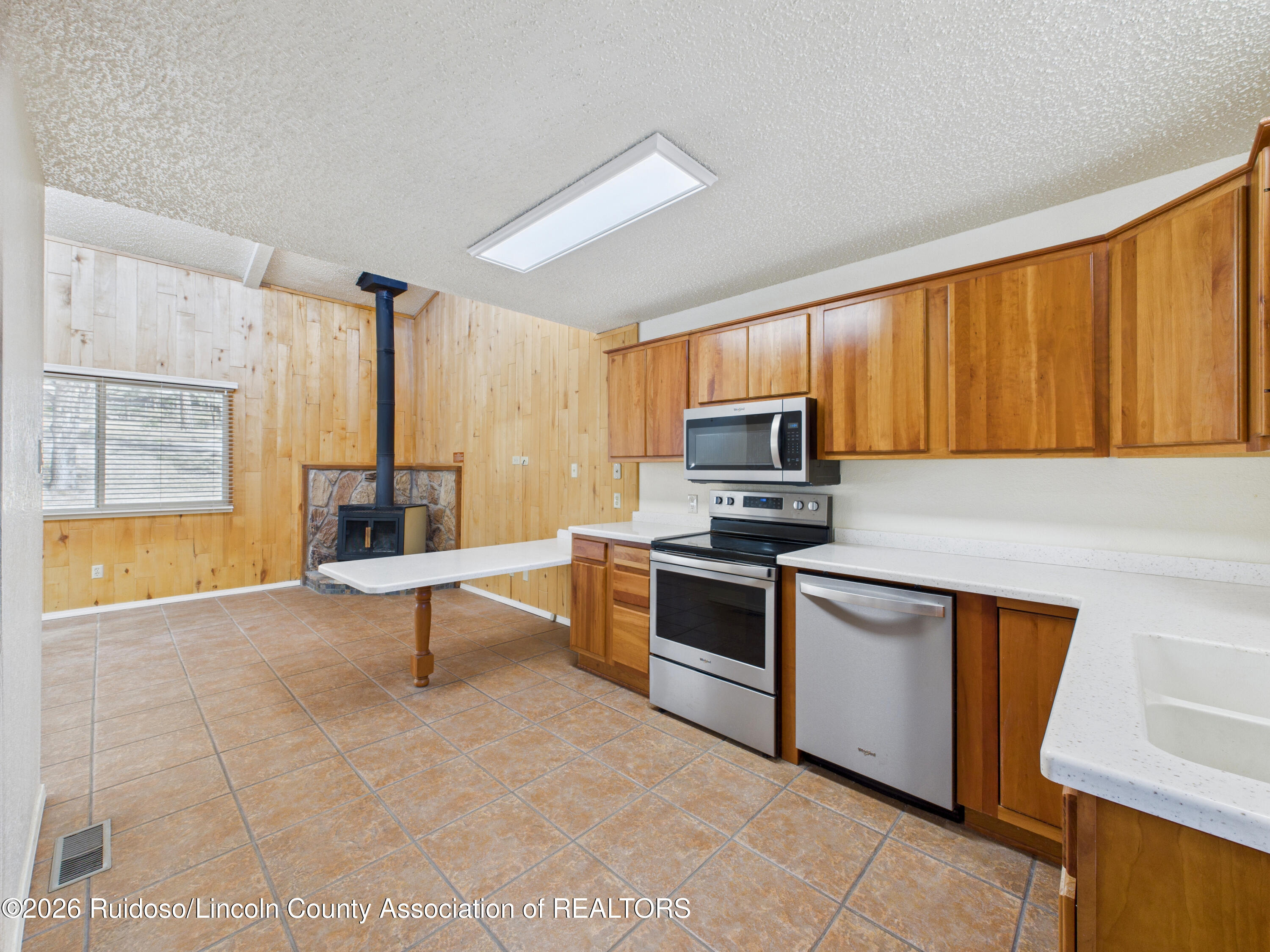 Kitchen with wood cabinetry, tiled floors, stainless steel appliances, and a wood stove.