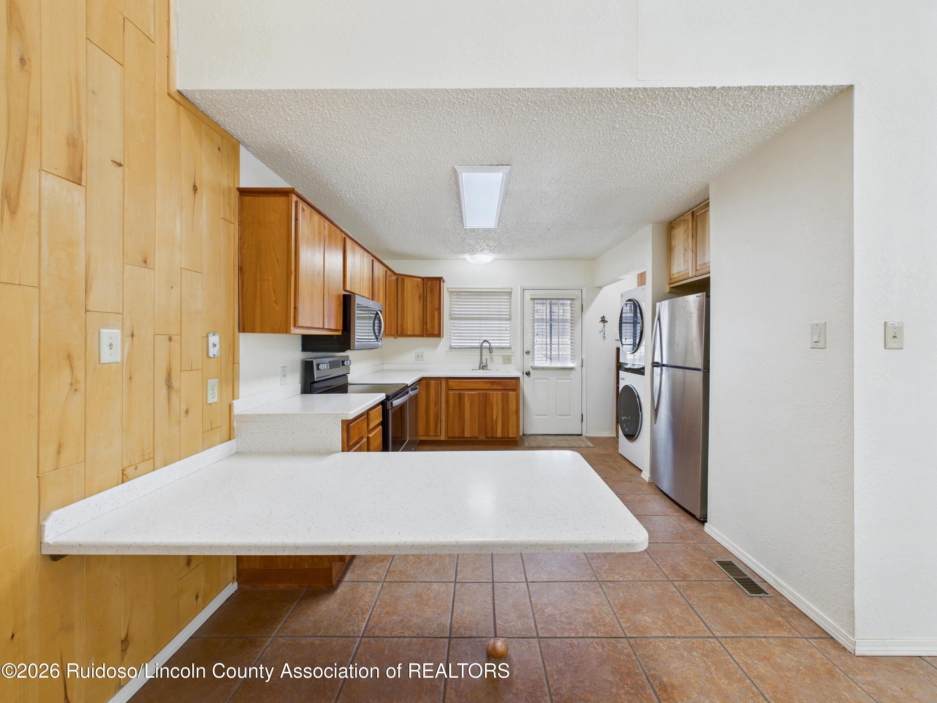 Kitchen with wood cabinets, white peninsula countertop, stainless appliances, and terracotta tile floor.