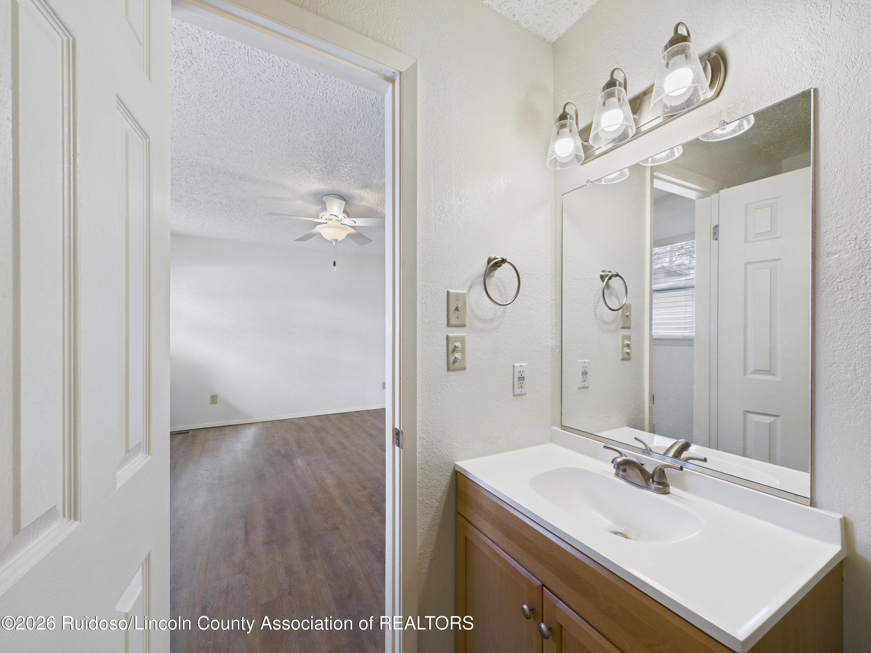 Bathroom vanity with a large mirror and three-bulb light, opening onto an unfurnished room.