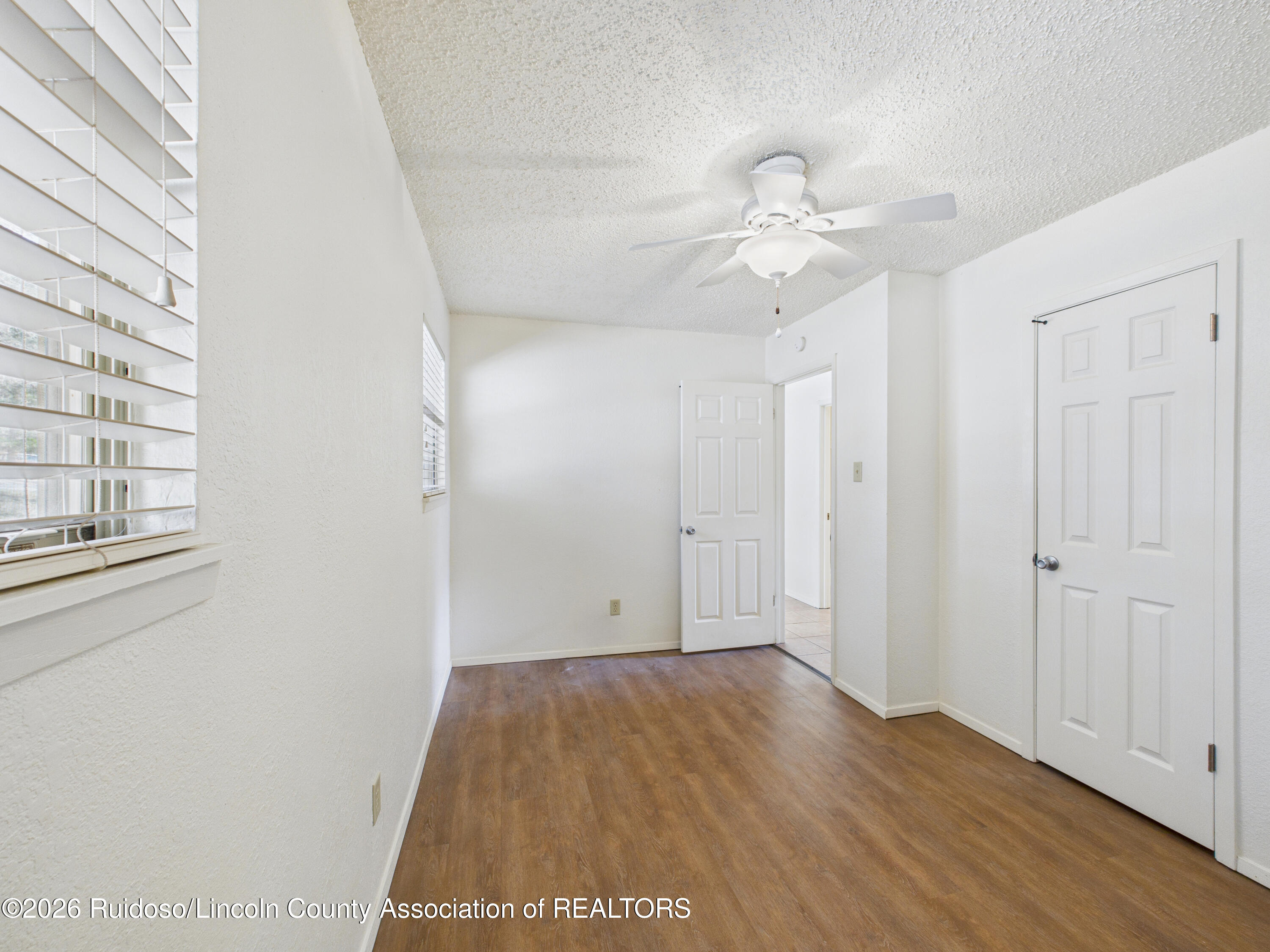 Empty room with wood-look flooring, window blinds, ceiling fan, and open doorway.