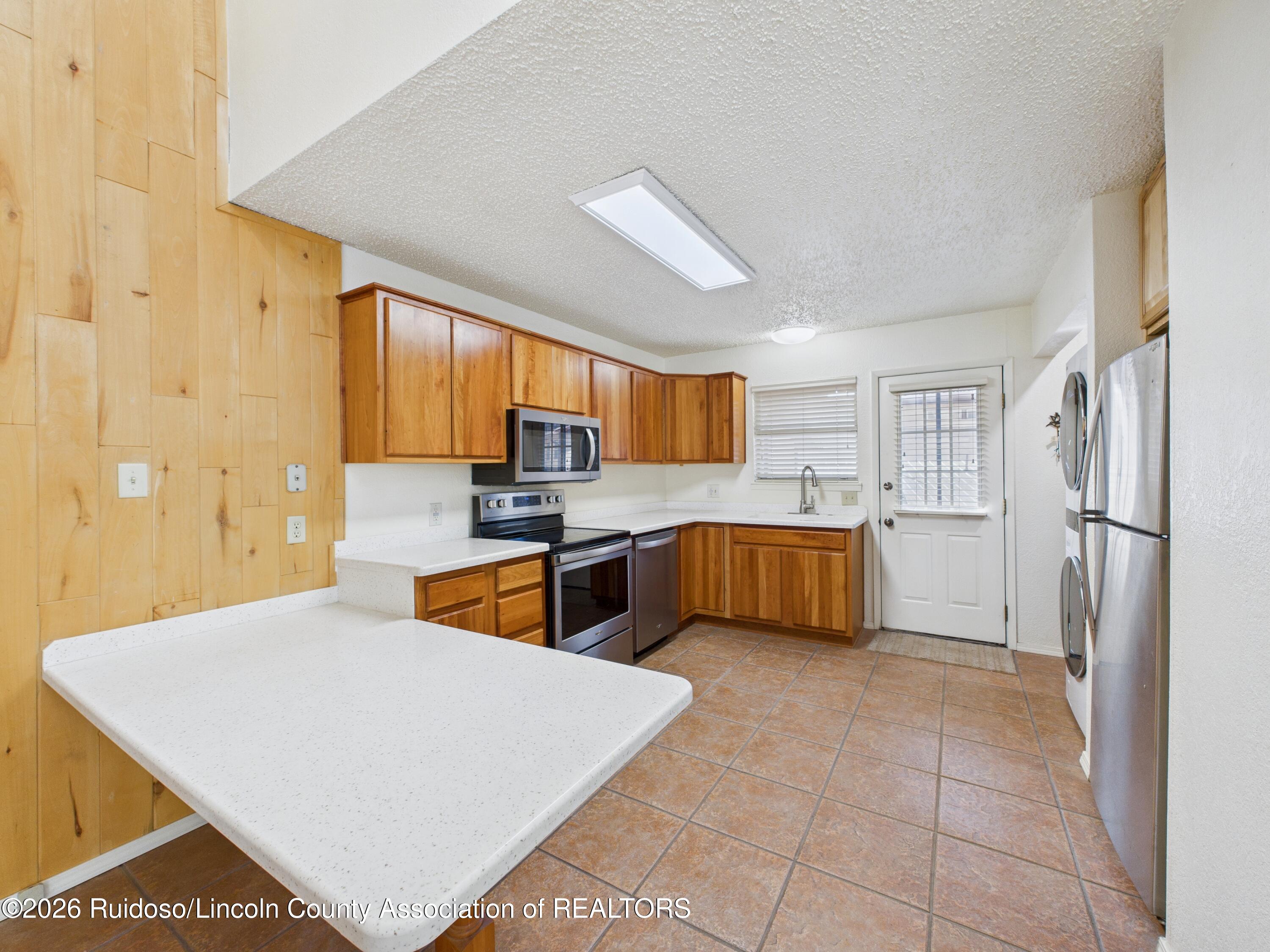 Kitchen with honey-toned wood cabinets, a spacious white peninsula, stainless steel appliances, and terracotta tile floors.
