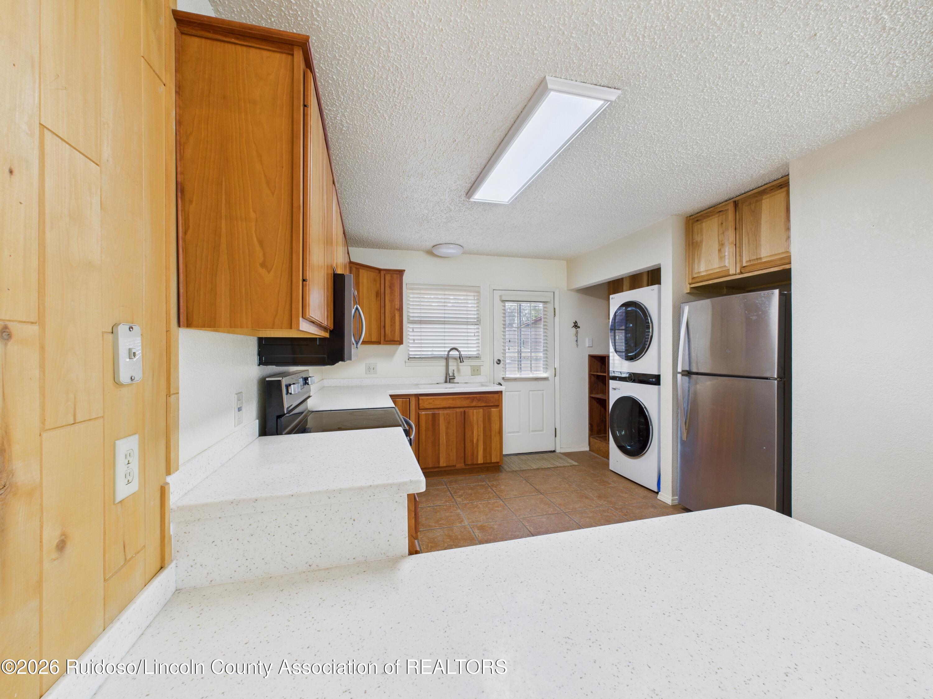Kitchen with wood cabinets, white counters, stainless-steel refrigerator, and stacked washer and dryer.