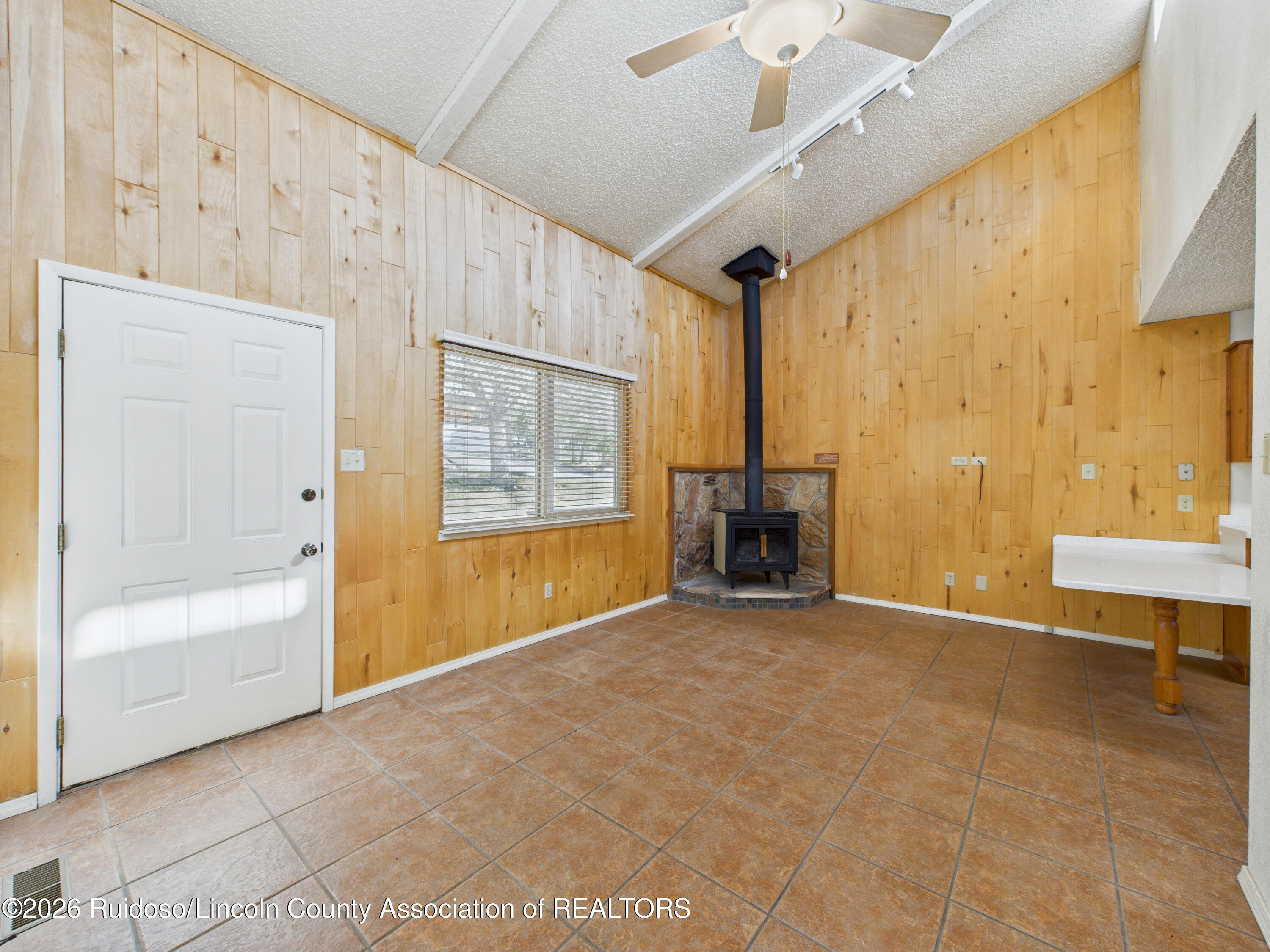 Empty wood-paneled room with a black wood stove, stone hearth, and brown tile floor.