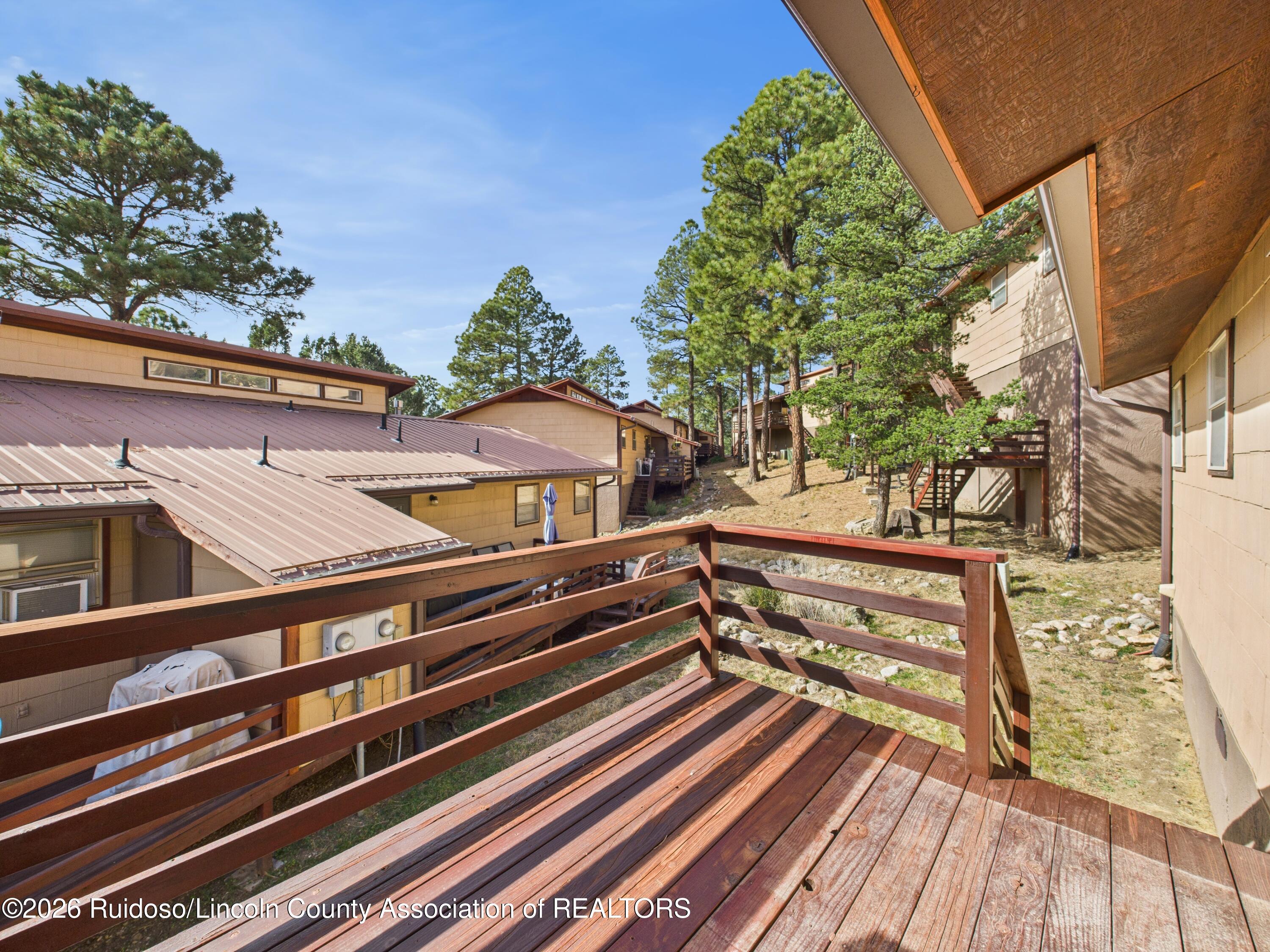 Wooden deck overlooking neighboring cabins and tall pine trees.