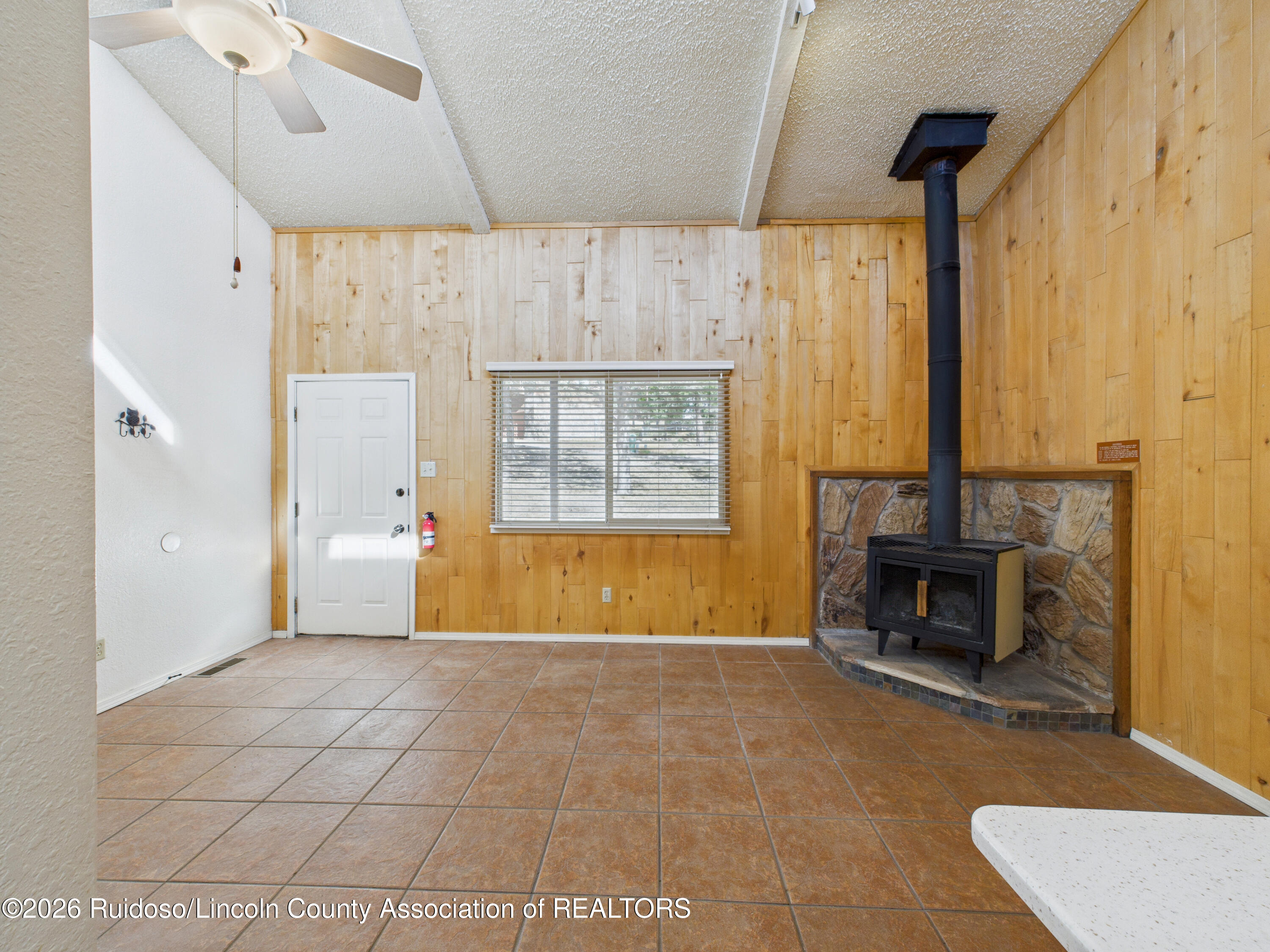Wood-paneled room with tiled floors and a freestanding wood stove against a stone surround.