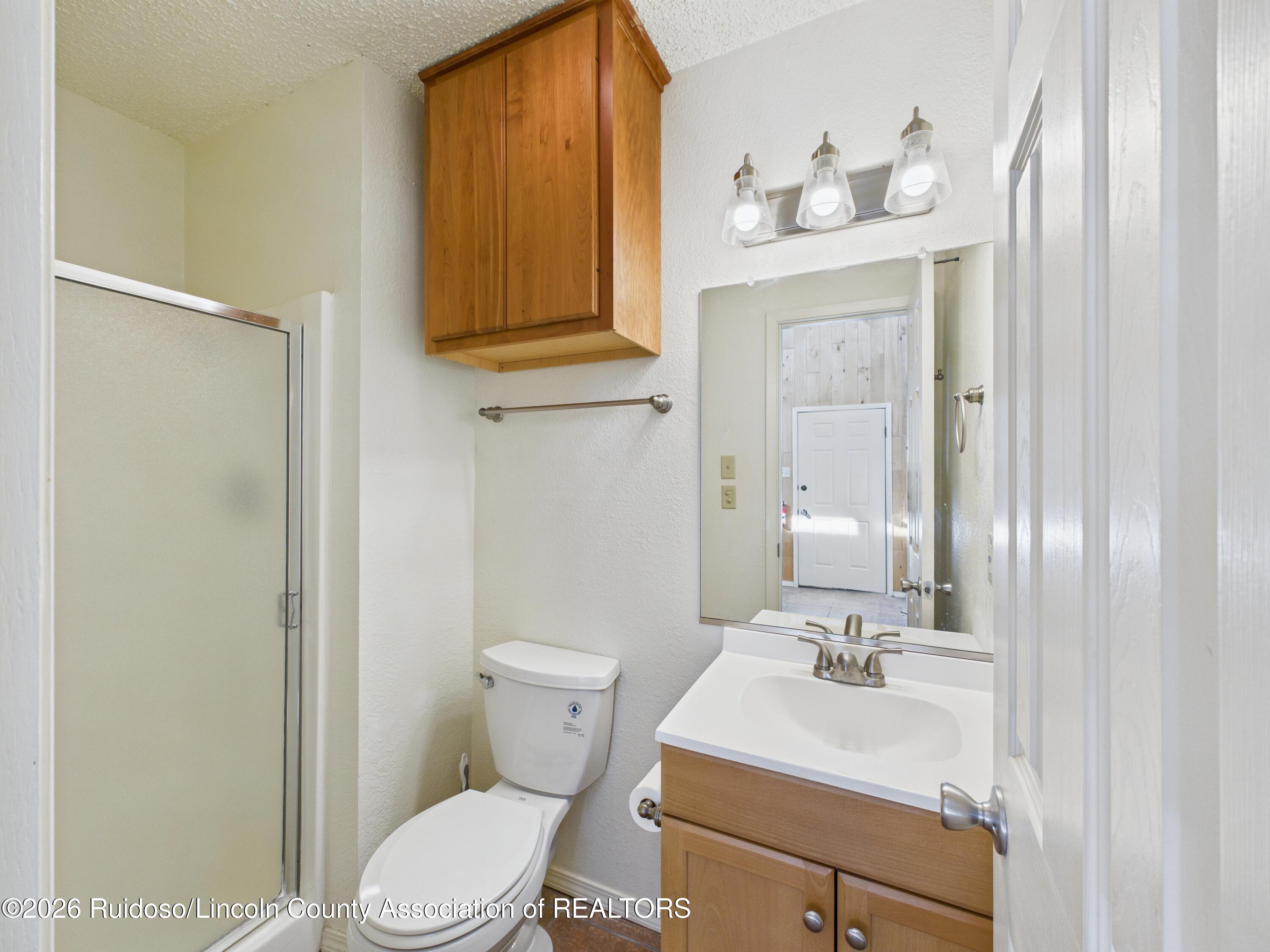 Bathroom with glass shower, toilet, and wood vanity beneath a large mirror.