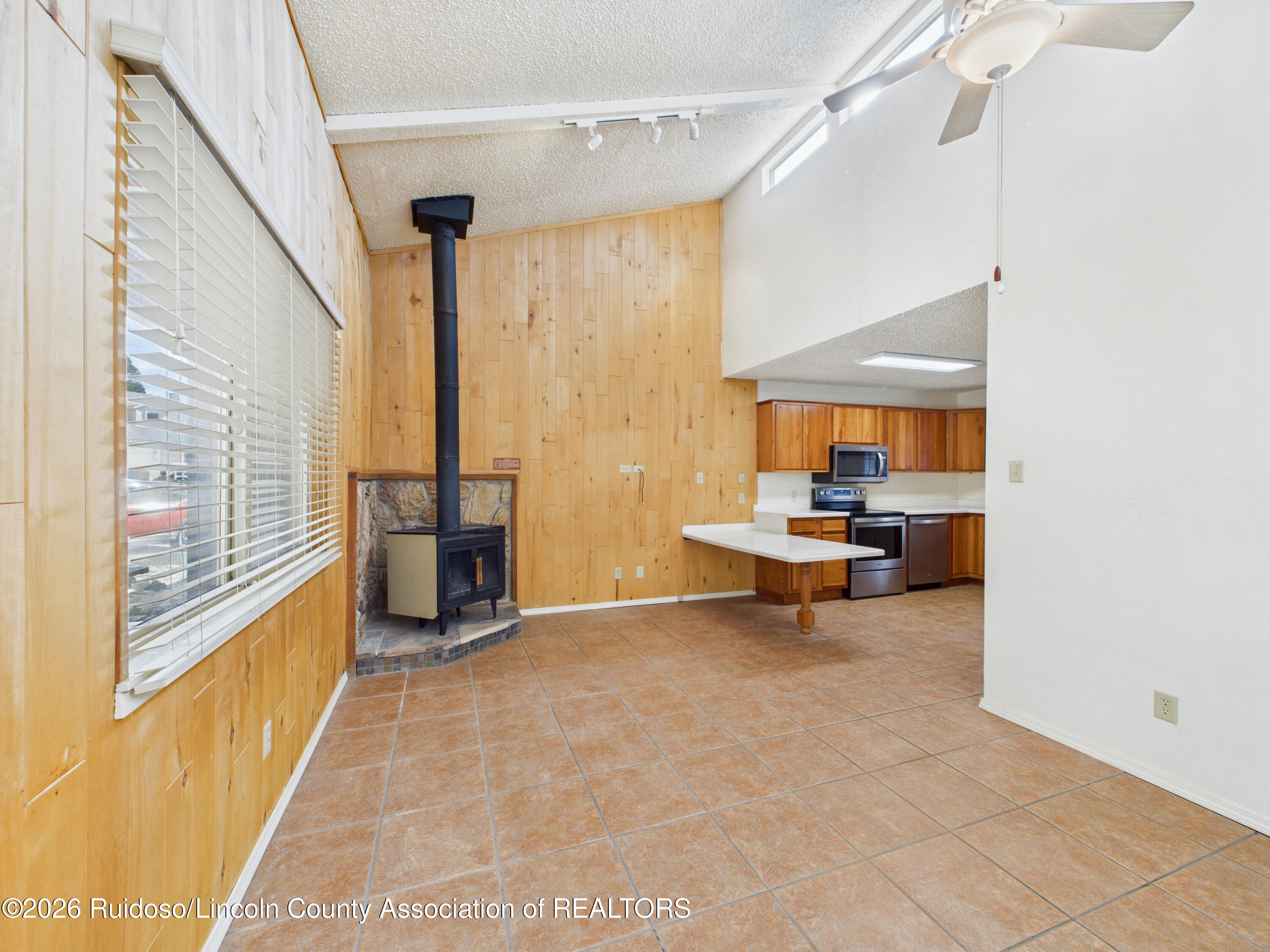 Open living and kitchen area with wood paneling, a freestanding stove, tile floors, and a breakfast peninsula.