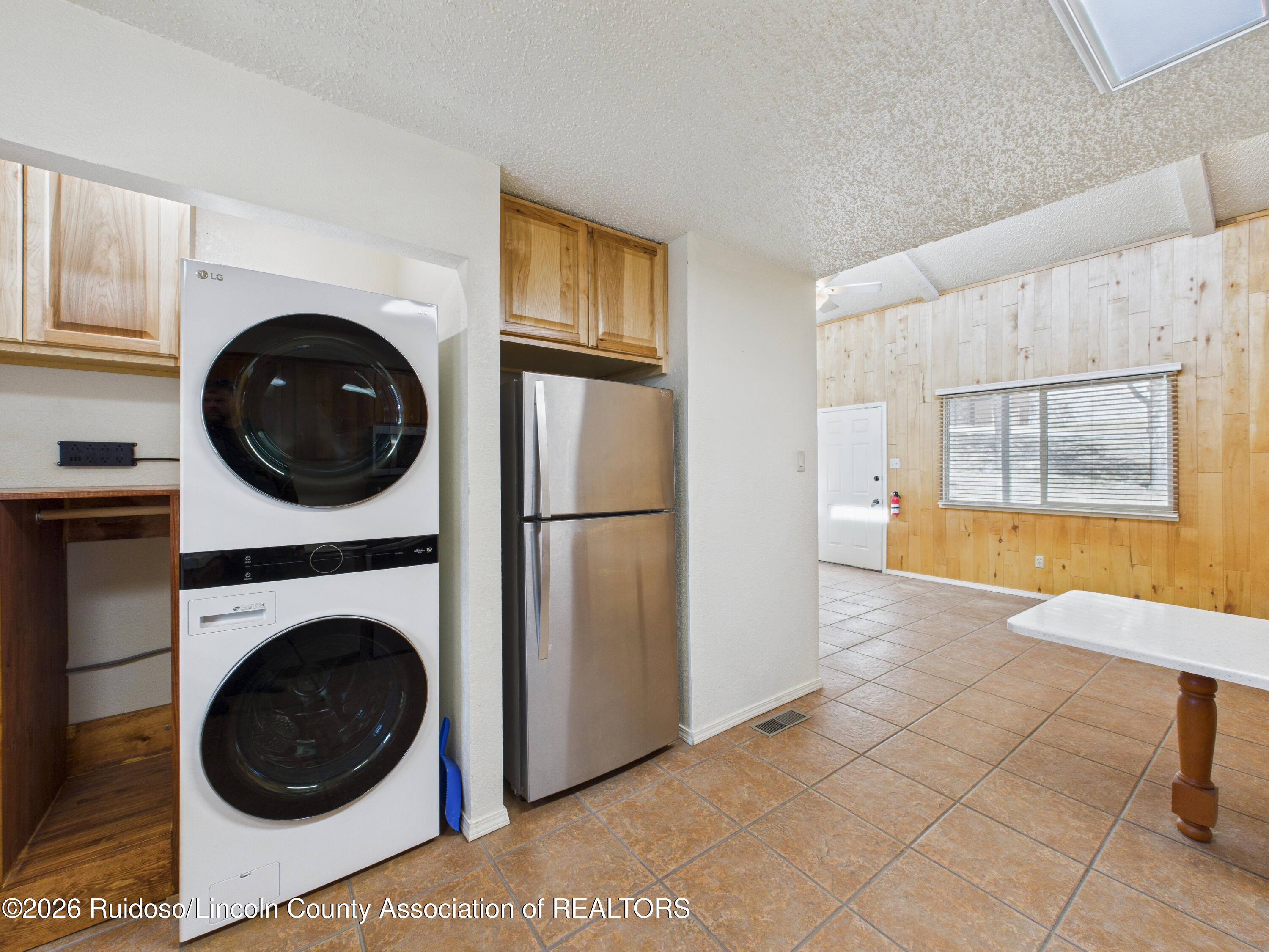 Kitchen and laundry area with stacked washer and dryer, stainless steel refrigerator, and wood-paneled walls.