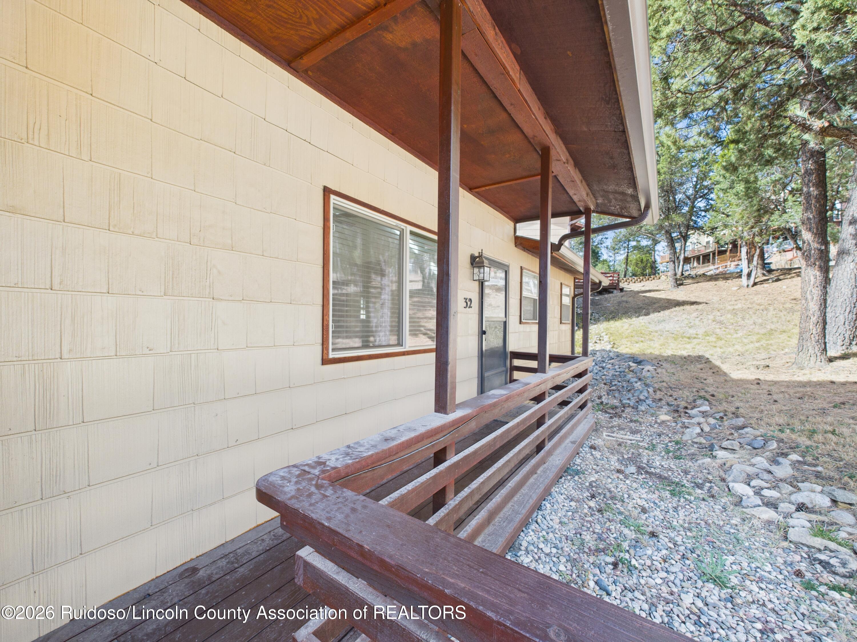 Unit 32’s covered wooden porch and entrance beside a rocky, tree-lined hillside.