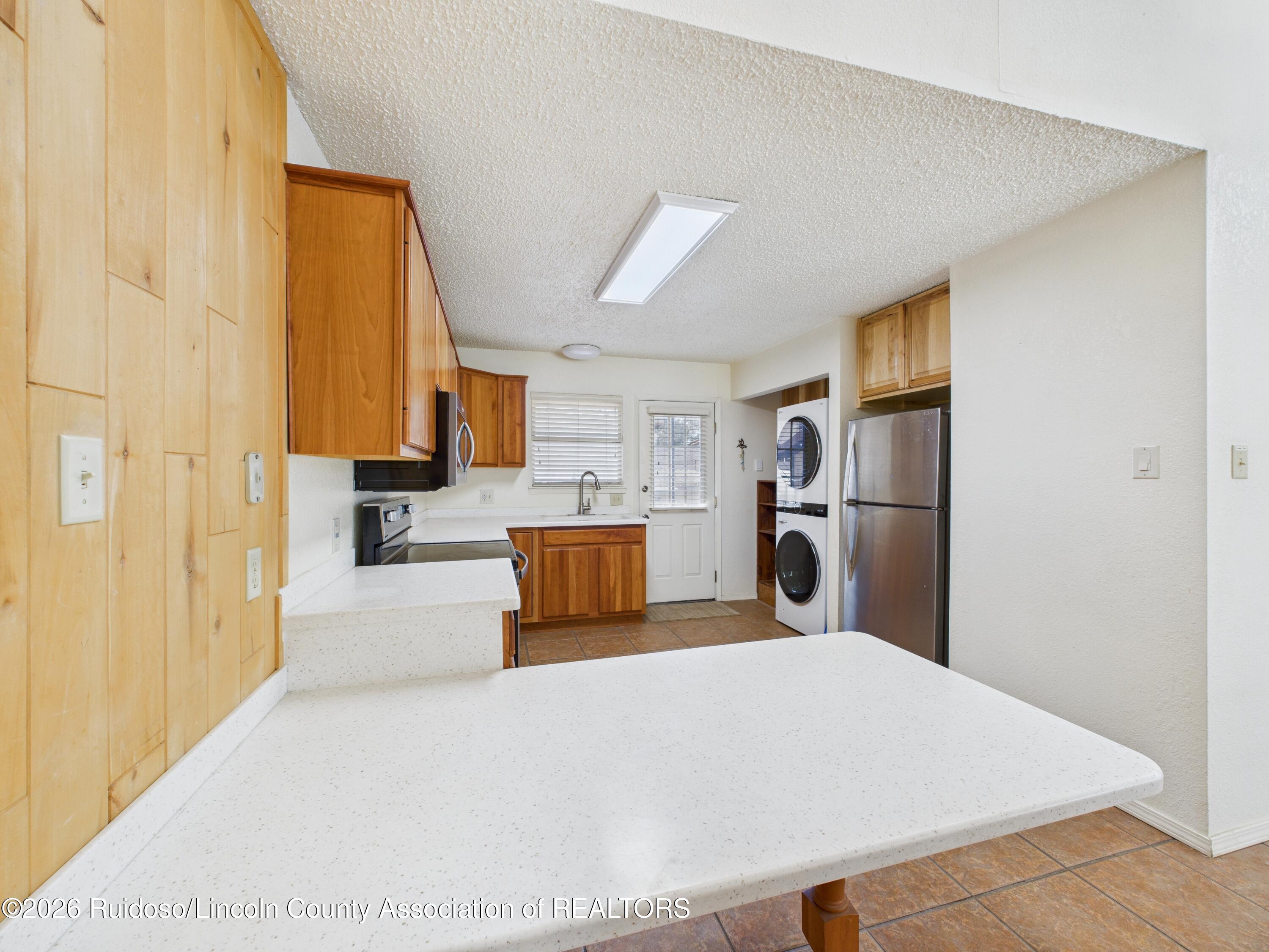 Kitchen with light wood cabinets, white counters, stainless refrigerator, and stacked washer and dryer.