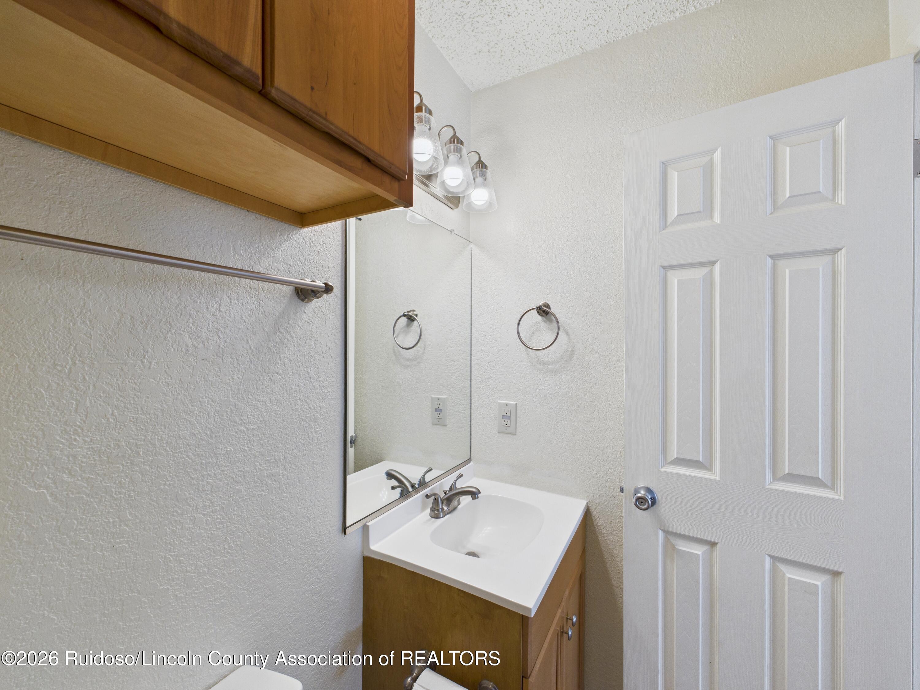 Bathroom vanity with a white sink, wood cabinetry, large mirror, and paneled door.