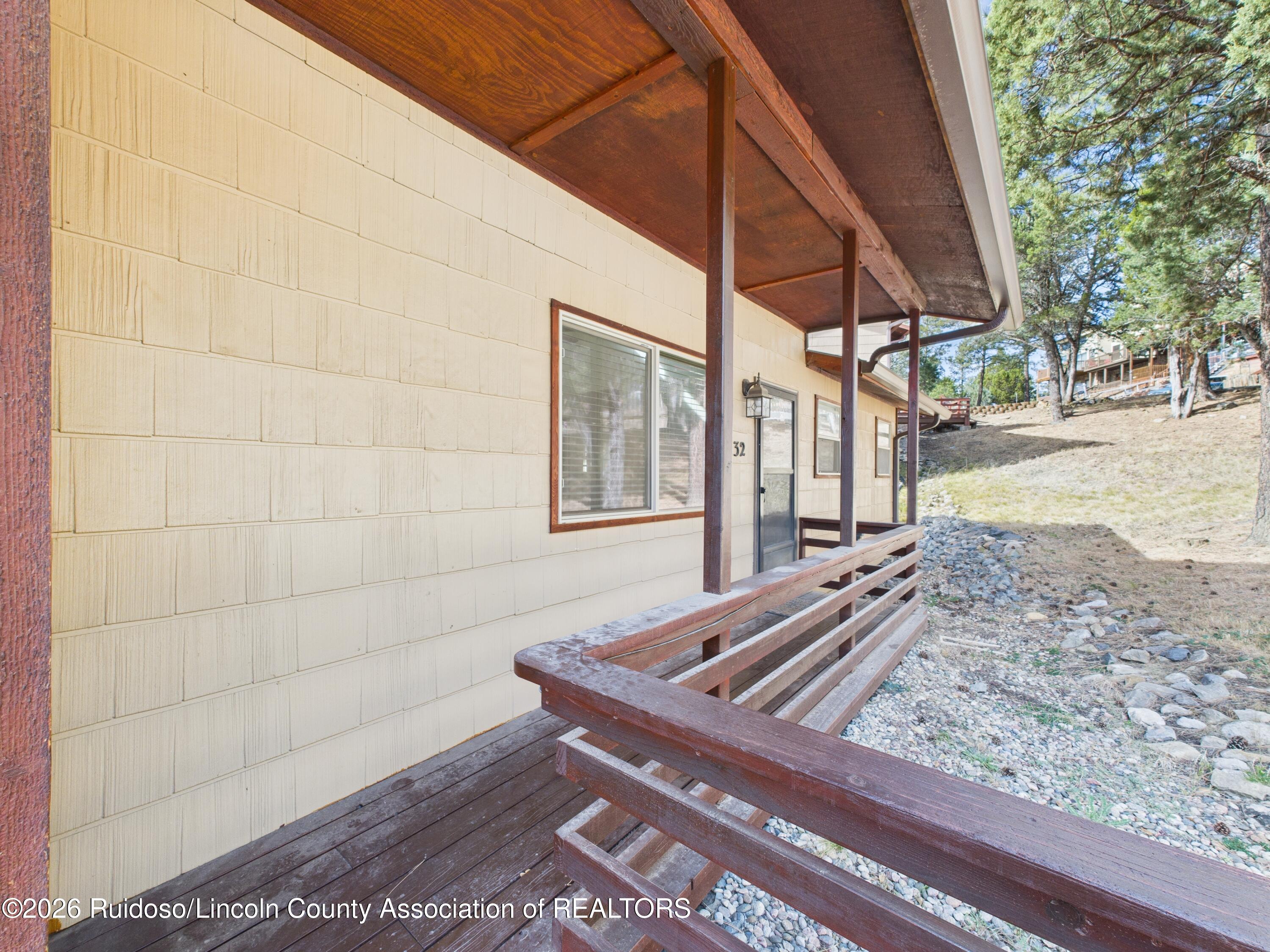 Unit 32’s covered wooden porch and glass entry door beside a rocky, pine-covered slope.
