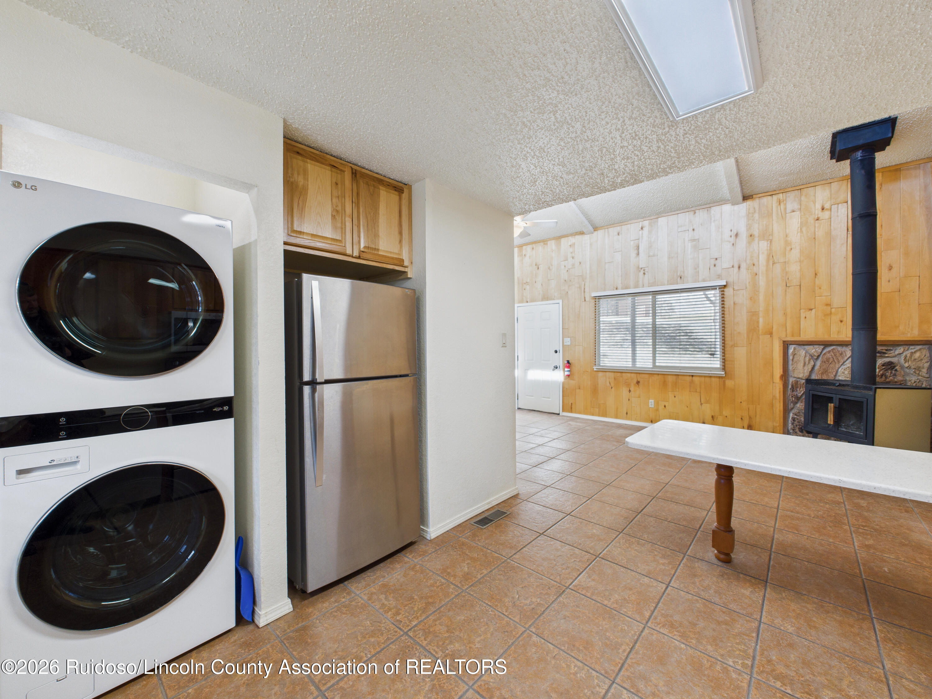 Kitchen with stacked washer and dryer, stainless refrigerator, wood-paneled walls, and a wood stove.