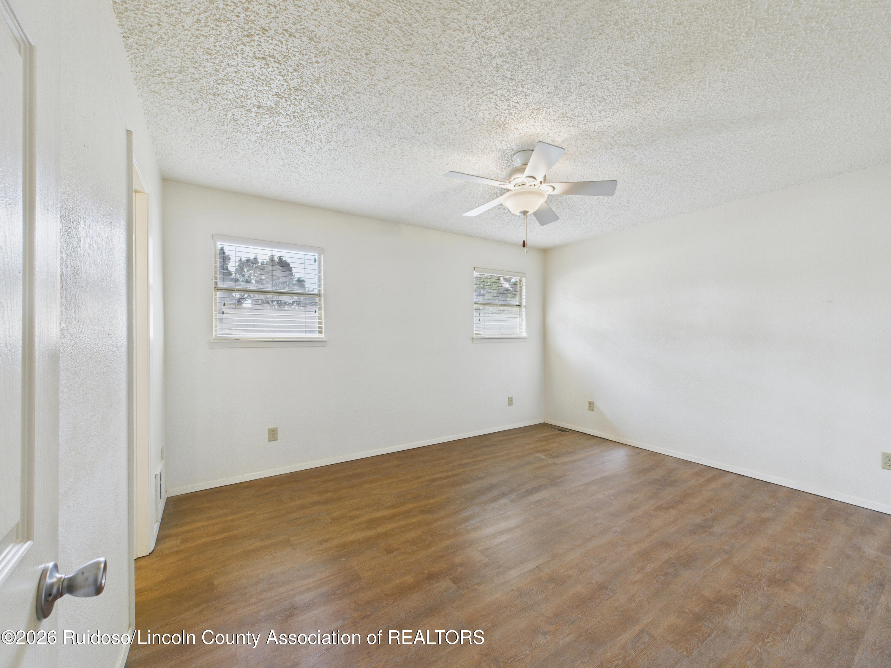 Empty room with wood-look flooring, two windows with blinds, and a ceiling fan.