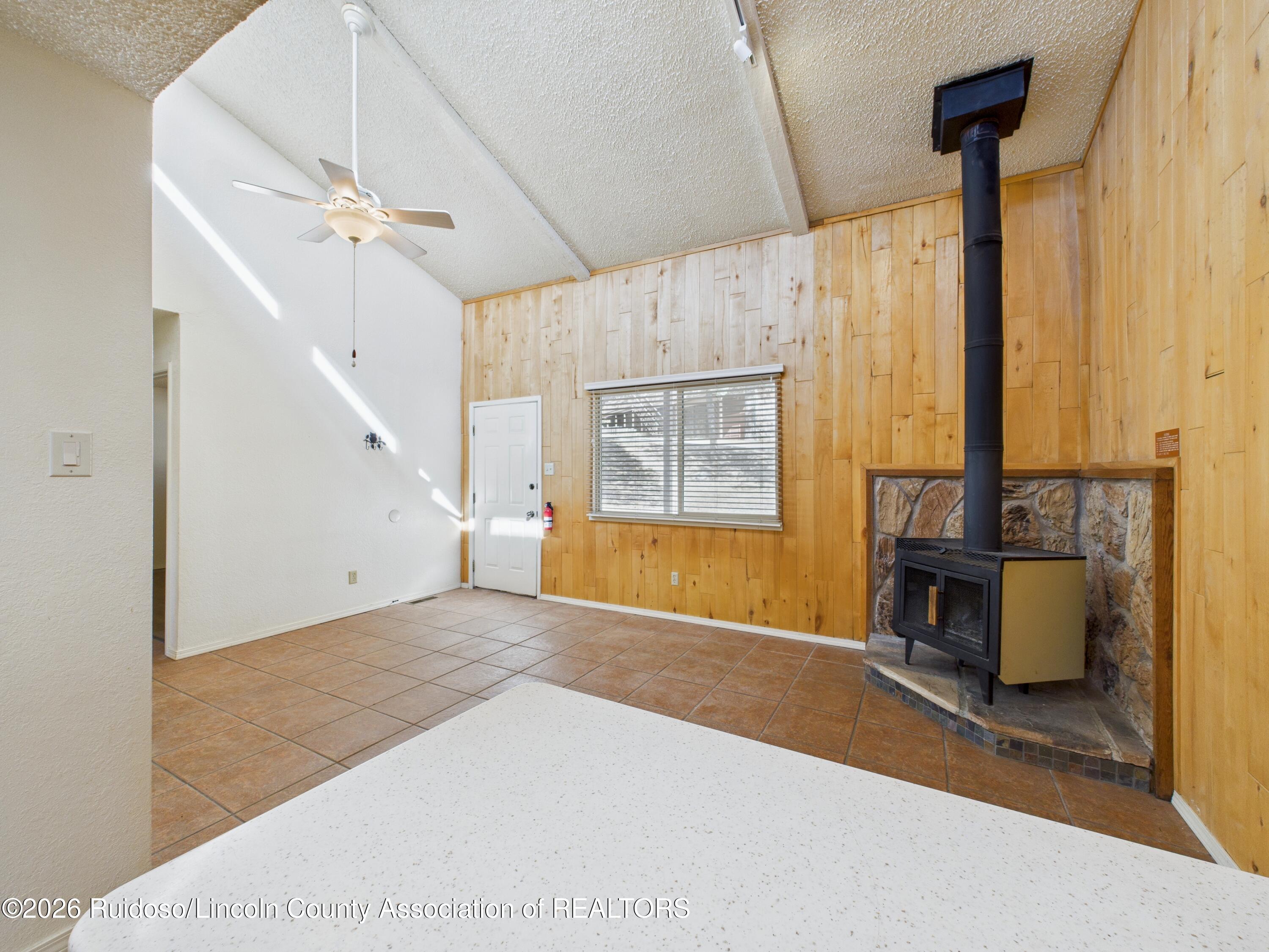 Vacant living room with wood-paneled walls, terracotta tile, and a freestanding stove beside a stone hearth.