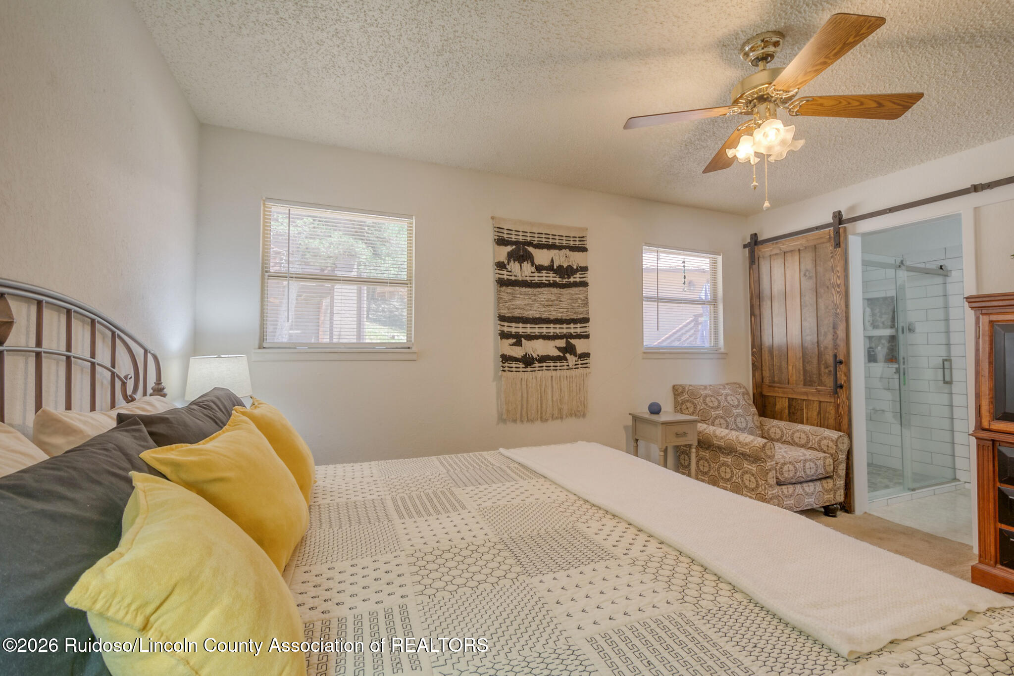 Furnished bedroom with patterned bedding, a wooden barn door, and an adjoining glass-enclosed shower.