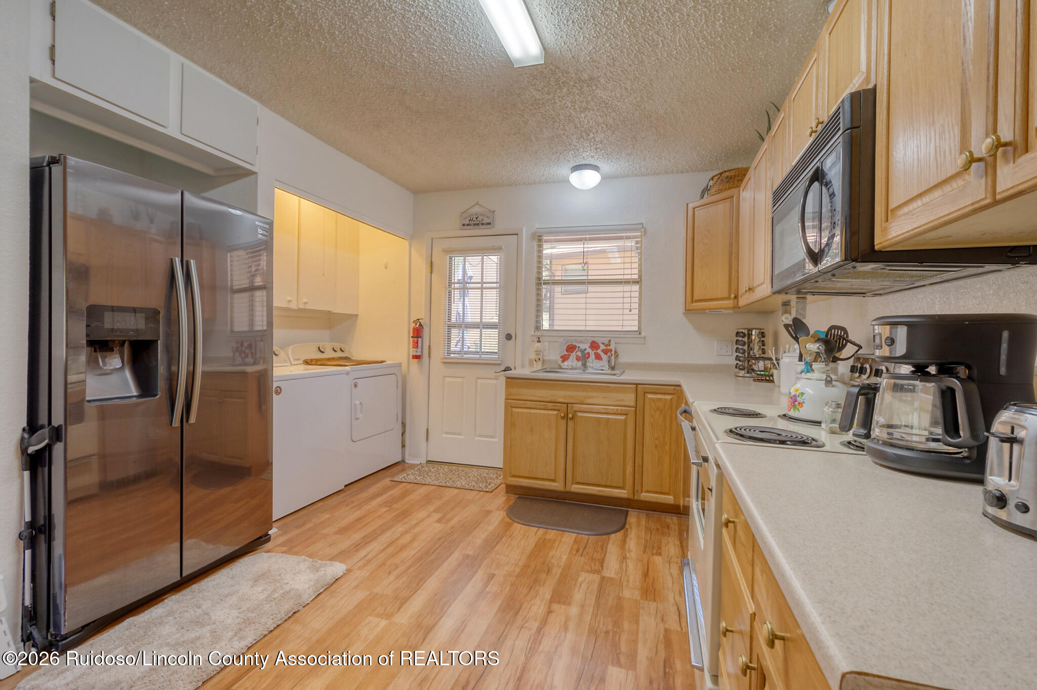 Kitchen with wood cabinets, stainless steel refrigerator, electric range, and washer and dryer.