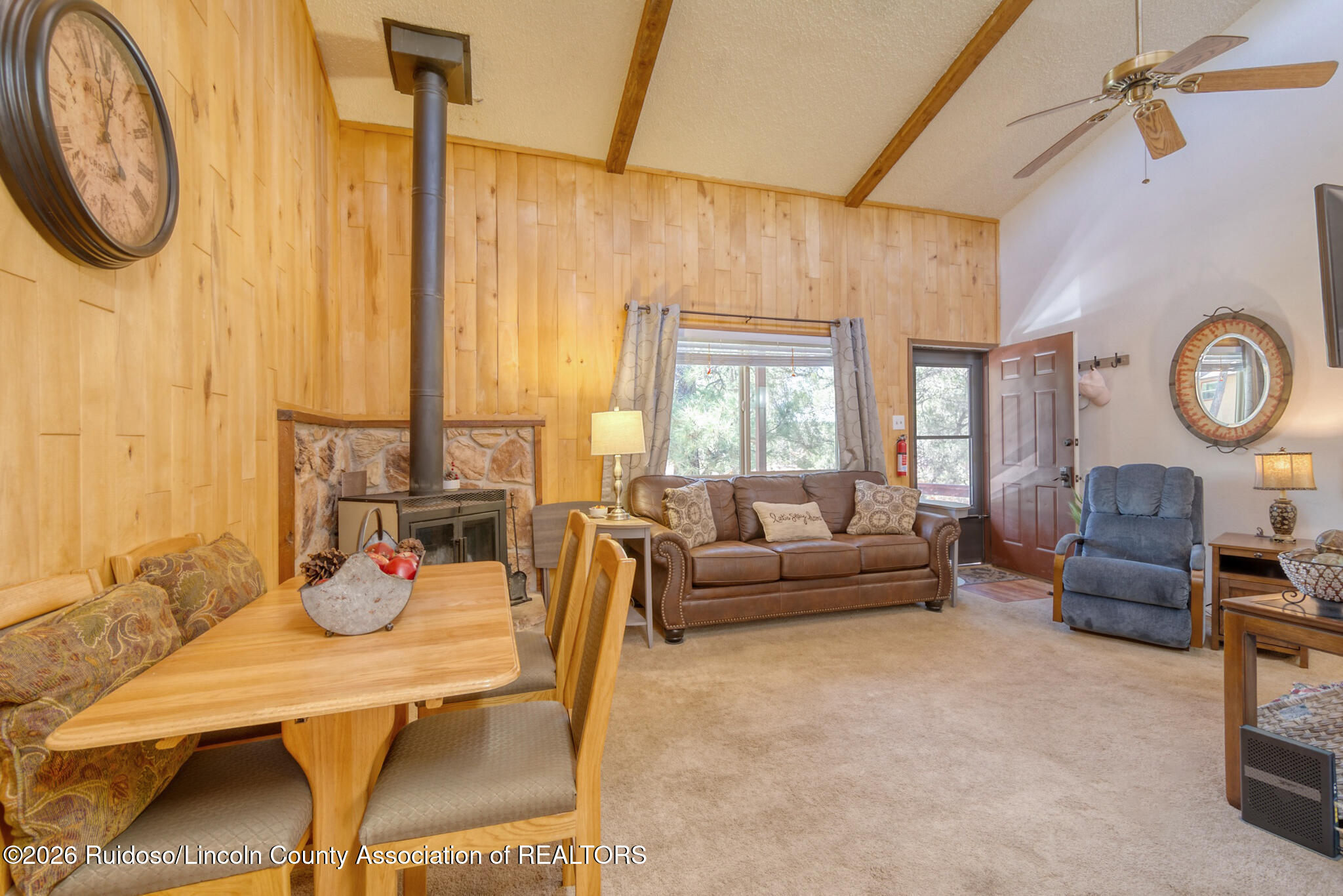 Furnished living room with a stone-backed wood stove, wood-paneled walls, and a brown leather sofa.