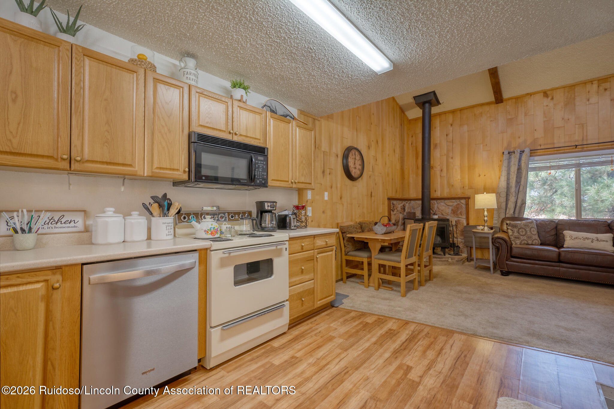 Kitchen and living area with wood cabinetry, dining nook, and a wood stove beside the sofa.