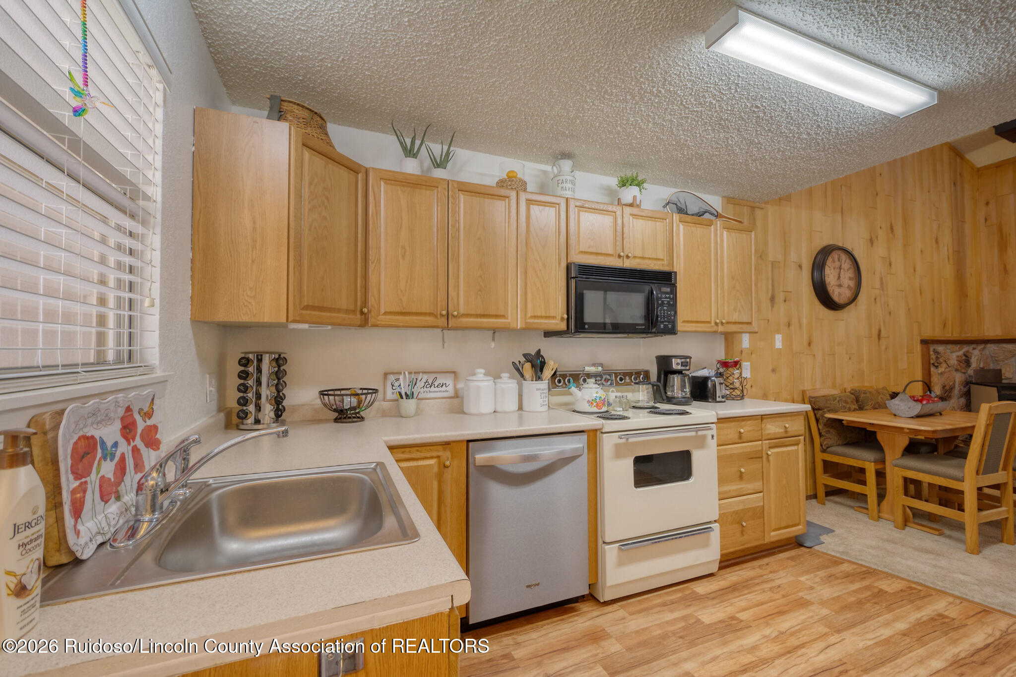 Kitchen with wood cabinets, a double-basin sink, white appliances, and an adjacent dining nook.