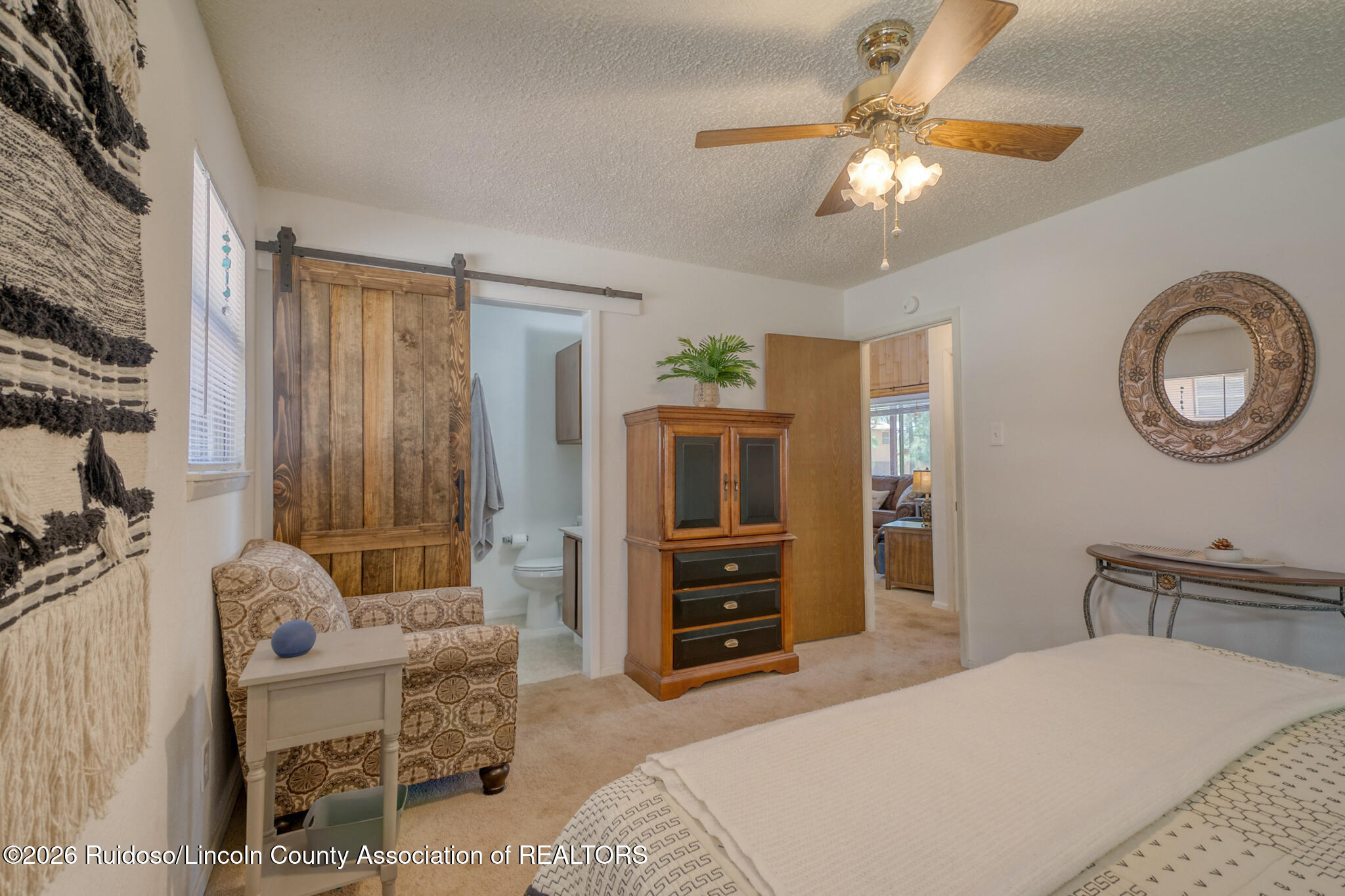 Furnished bedroom with a wooden barn door opening to an ensuite bathroom and a patterned armchair.