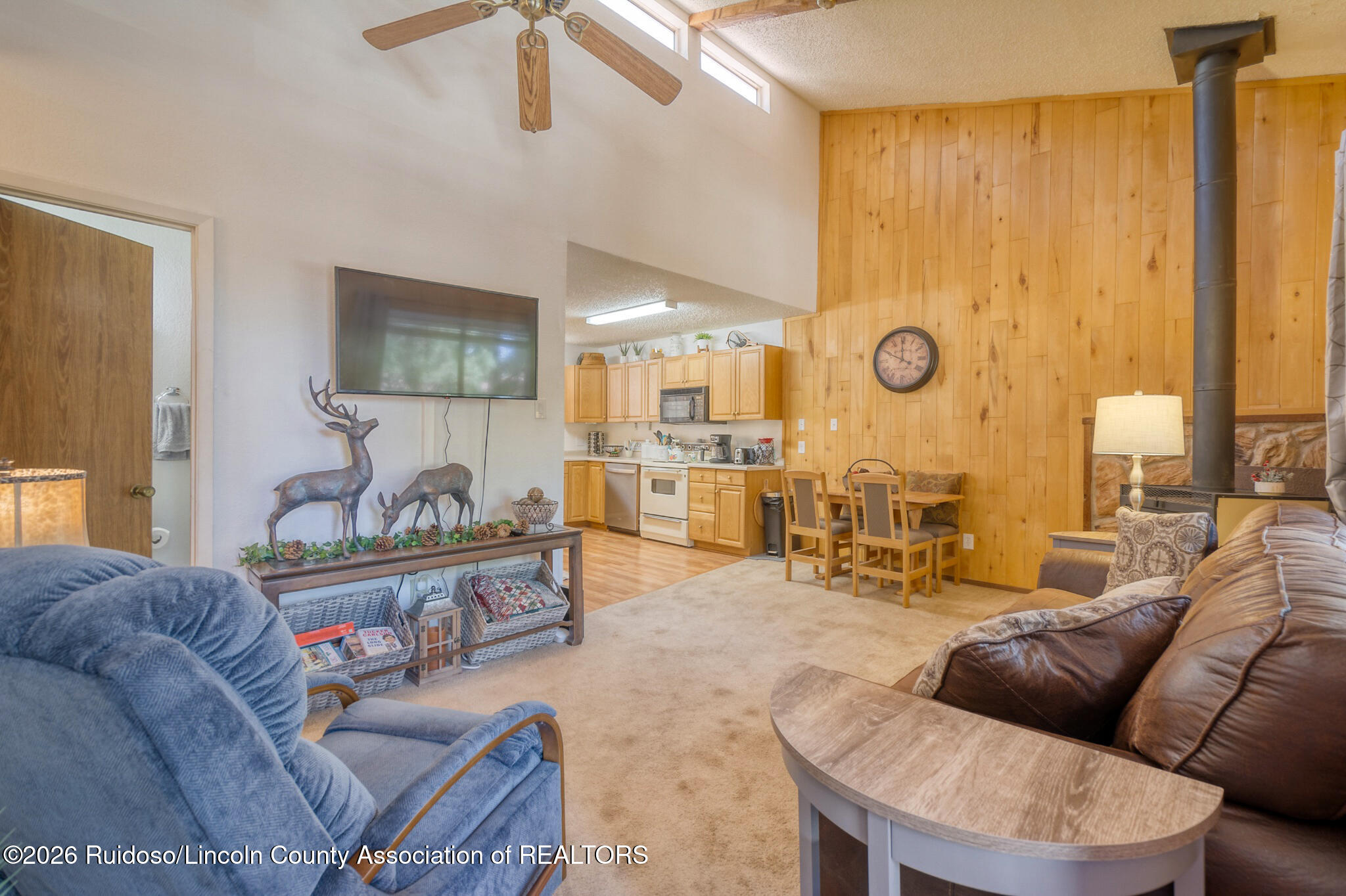 Living room with a blue recliner, leather sofa, and open kitchen against wood-paneled walls.