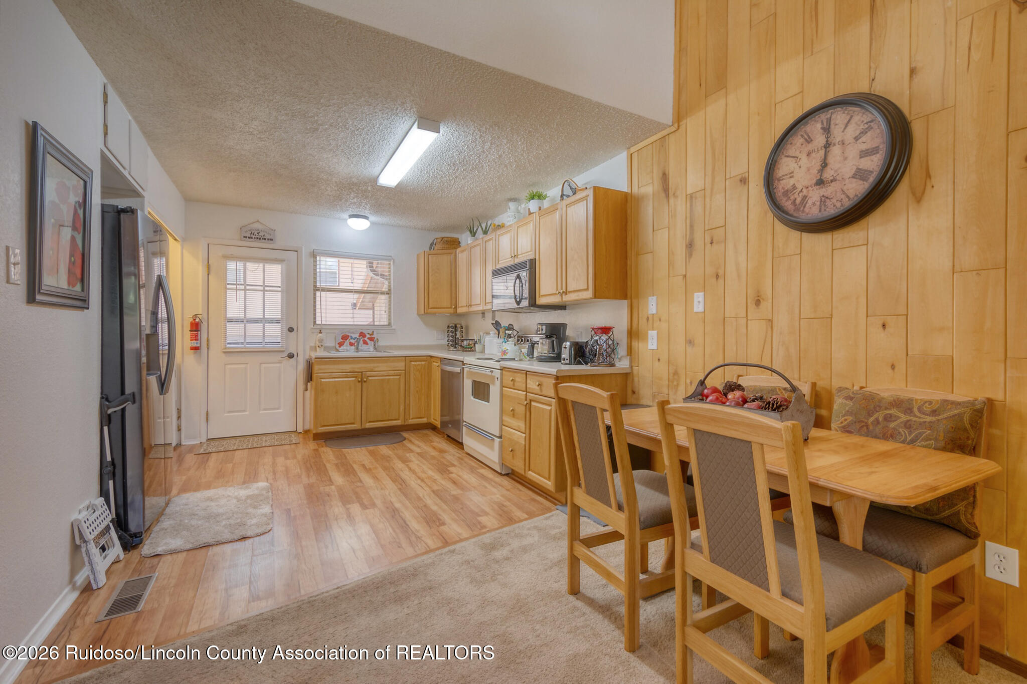 Kitchen and dining area with wood cabinets, paneled walls, and a wooden table with cushioned chairs.